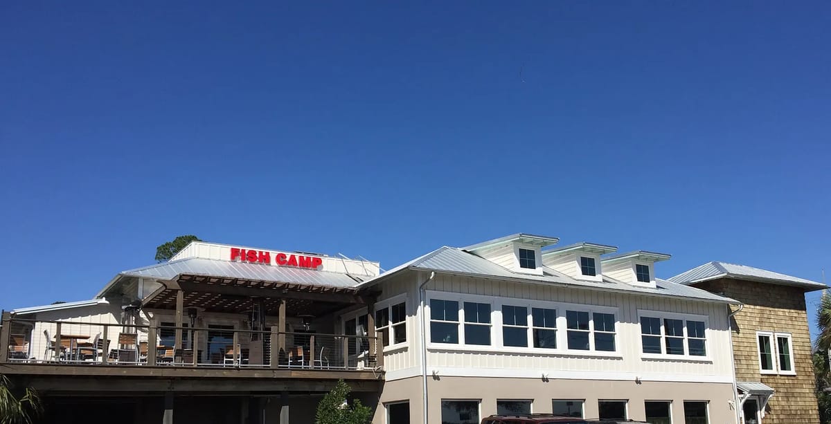 Exterior of a restaurant named 'FISH CAMP' with deck area, multiple windows, and pitched roofs