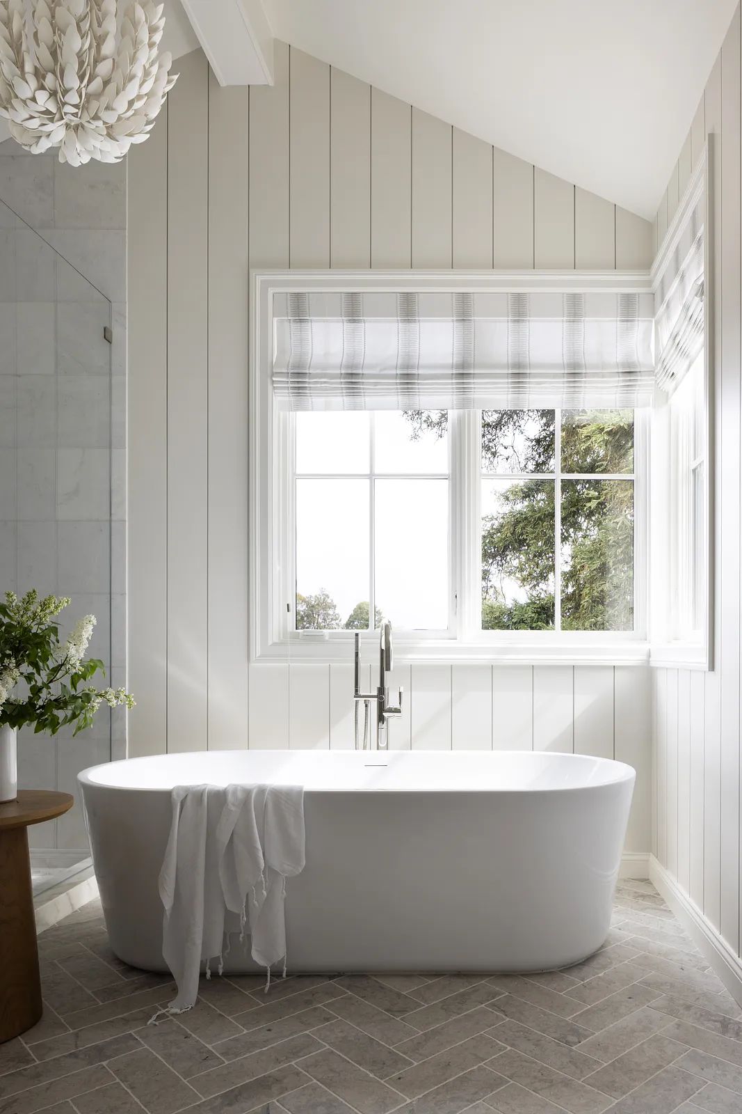 Bathroom with freestanding white bathtub, wooden side table, plaid window shades, and shiplap walls