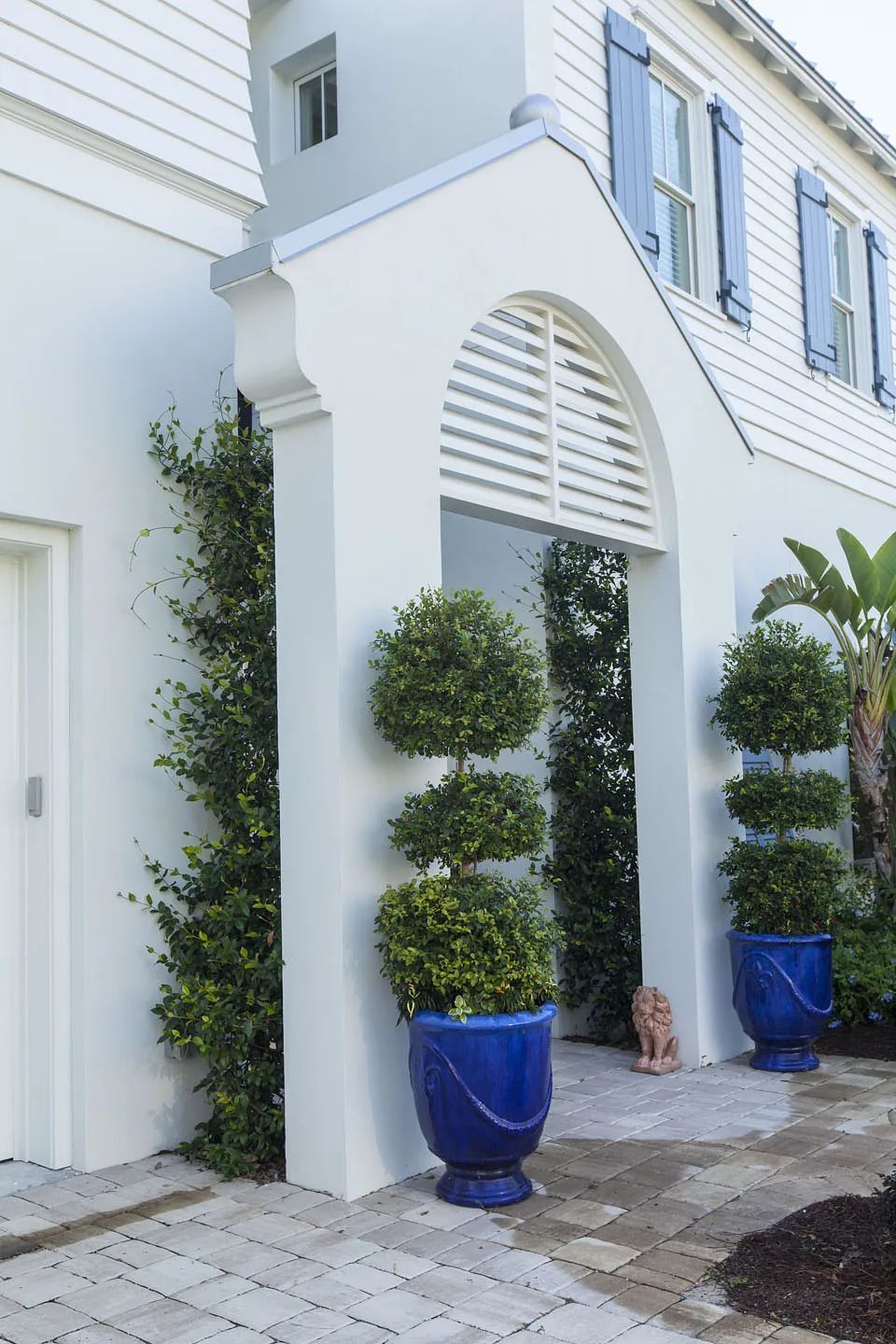 Exterior front with white wall, arched entrance, blue planters, shrubs, and decorative lion statue.