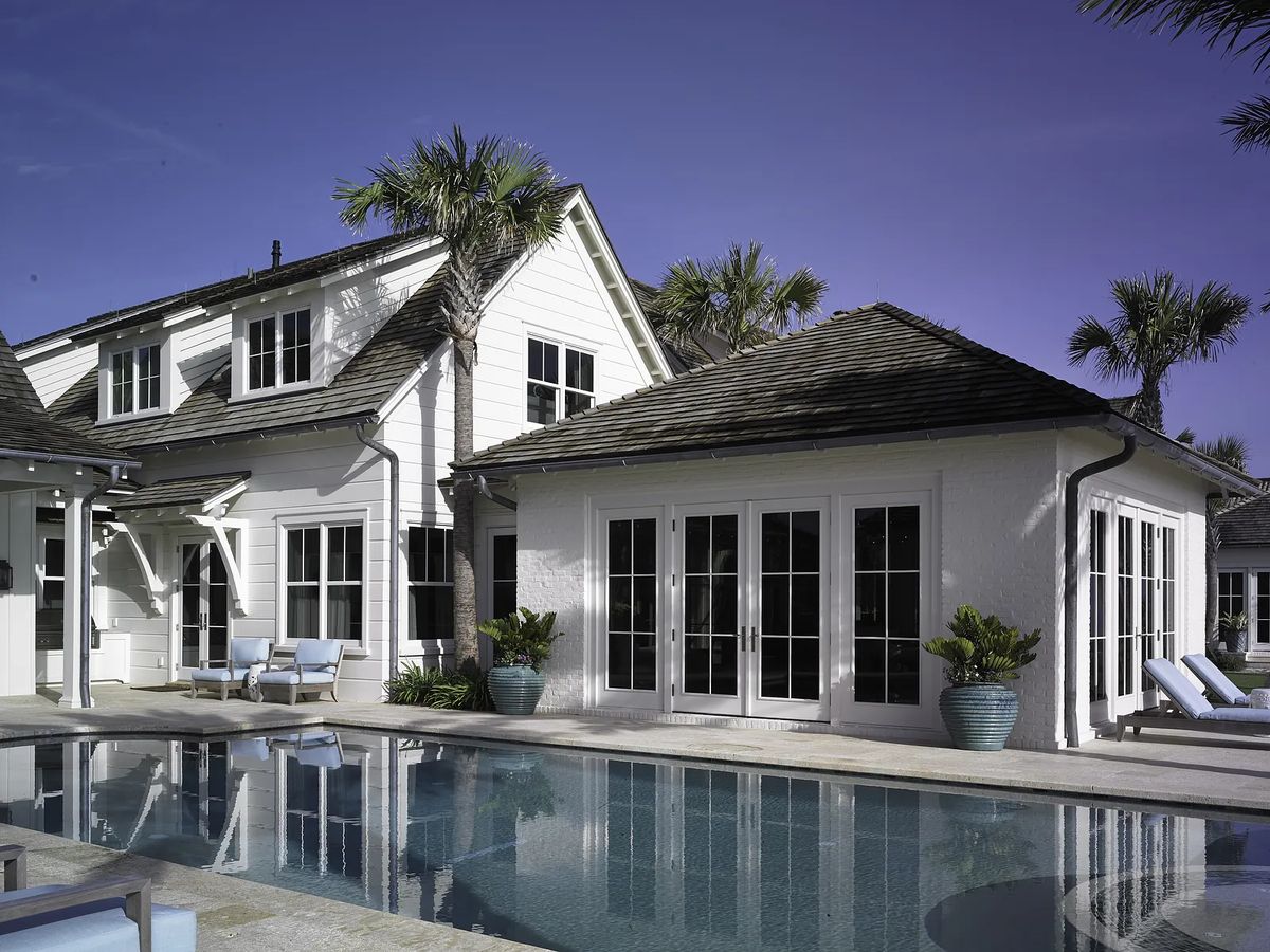 Exterior rear view of house with pool, deck, palm trees, and large windows.