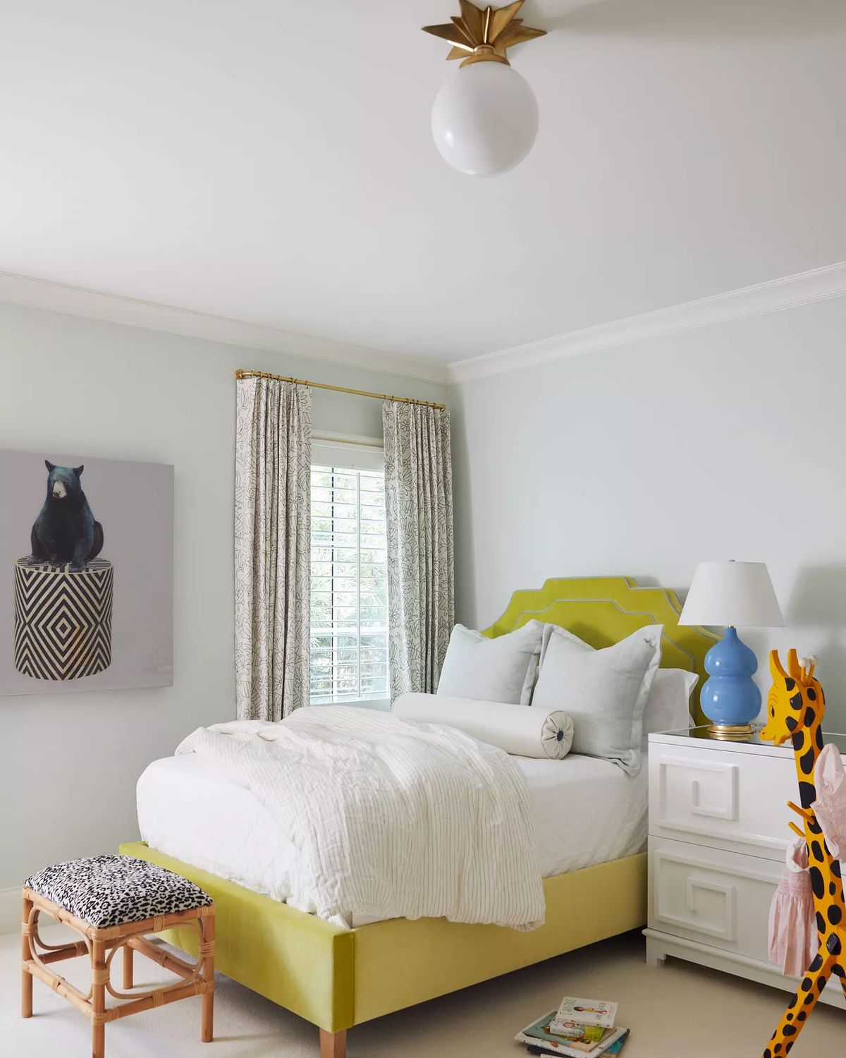 Bedroom with green bed, white blanket, nightstand, blue lamp, small stool, and bird artwork on the wall.