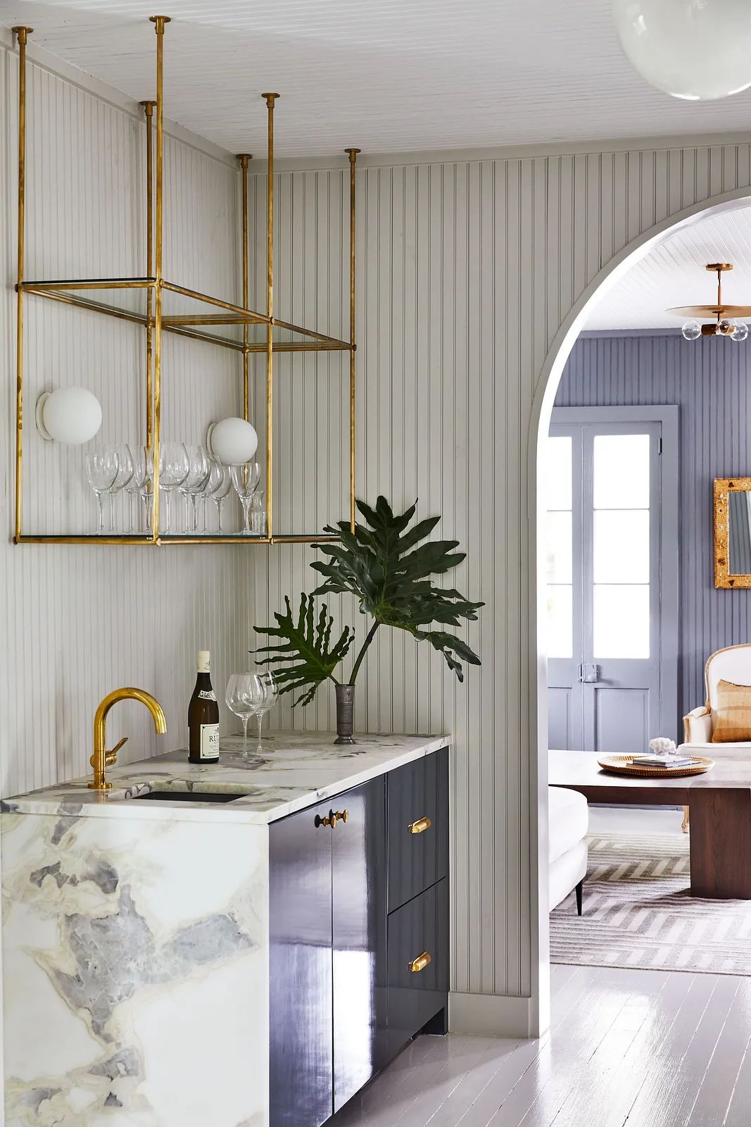 Kitchen with marble countertop, dark cabinetry, gold hardware, open shelving, and an archway to another room.