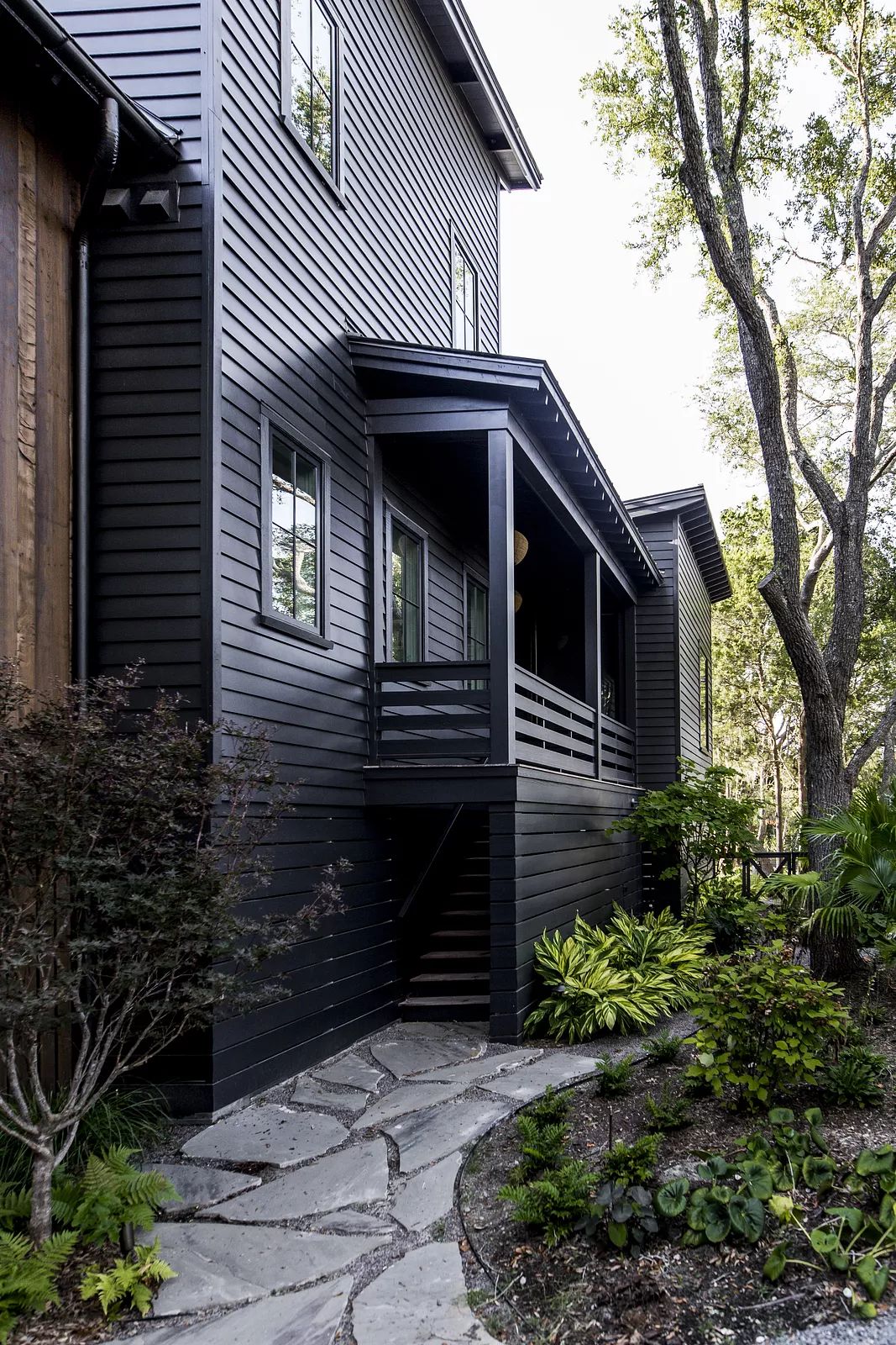 Exterior front view of a house with dark siding, porch, stone pathway, and surrounding greenery.