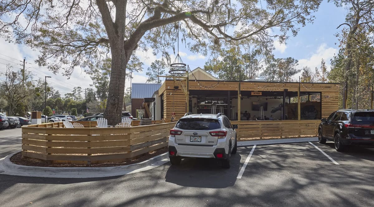 Exterior front view with wooden fencing, parking area, and large tree adjacent to the building.
