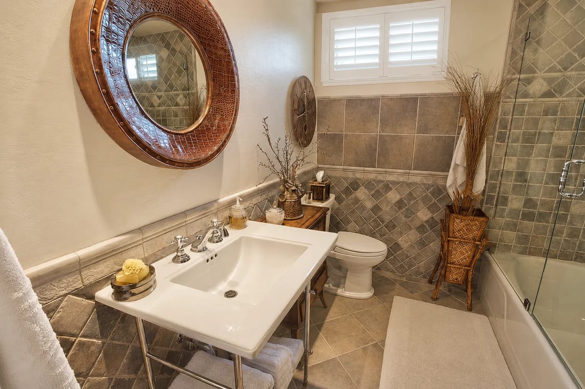 Bathroom with white sink, toilet, bathtub, round mirror, and patterned tile walls.