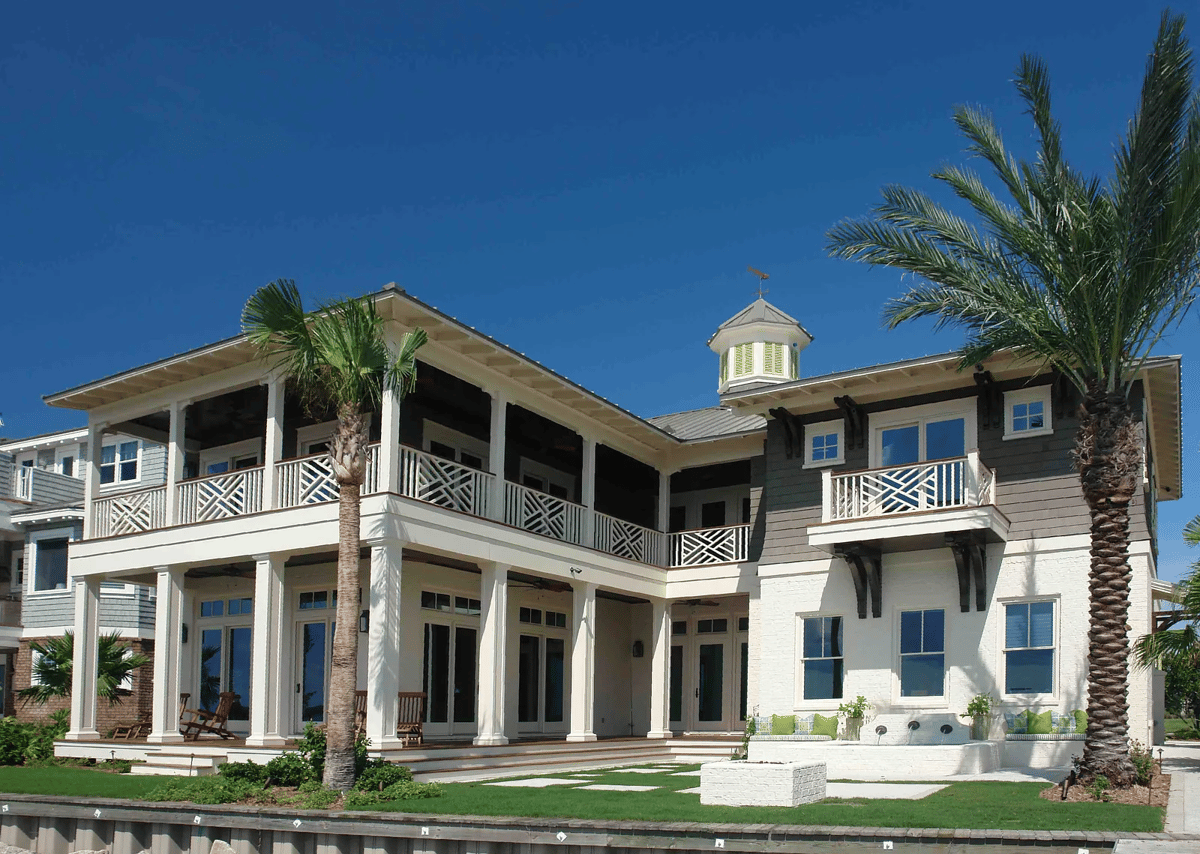 Exterior front view of a multi-story house with white and gray siding, porch, and palm trees.