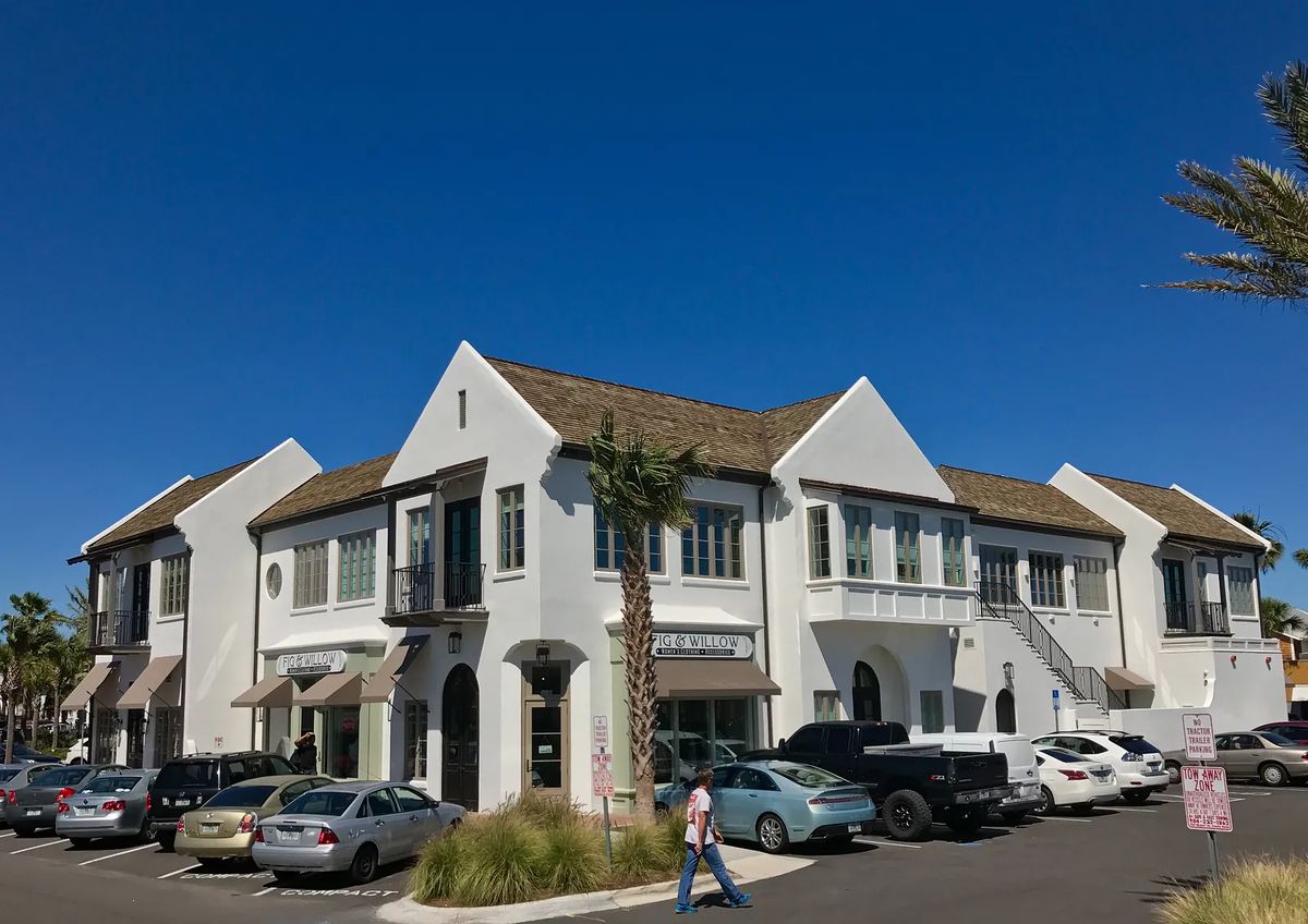 Commercial building with white stucco facade, tiled roof, large windows, and paved parking.