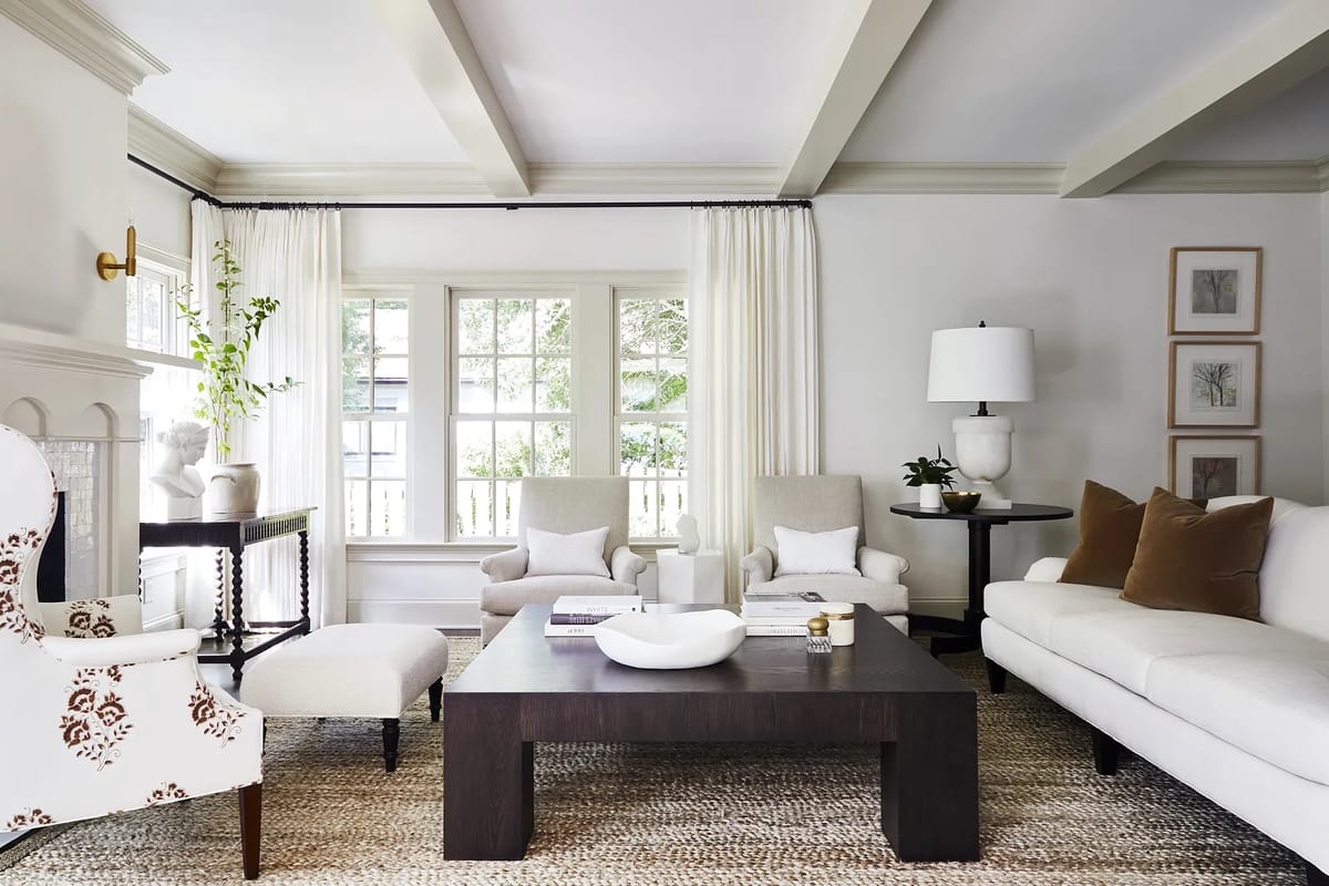 Living room with white sofa, wooden coffee table, armchairs, area rug, large windows, and floor lamp.