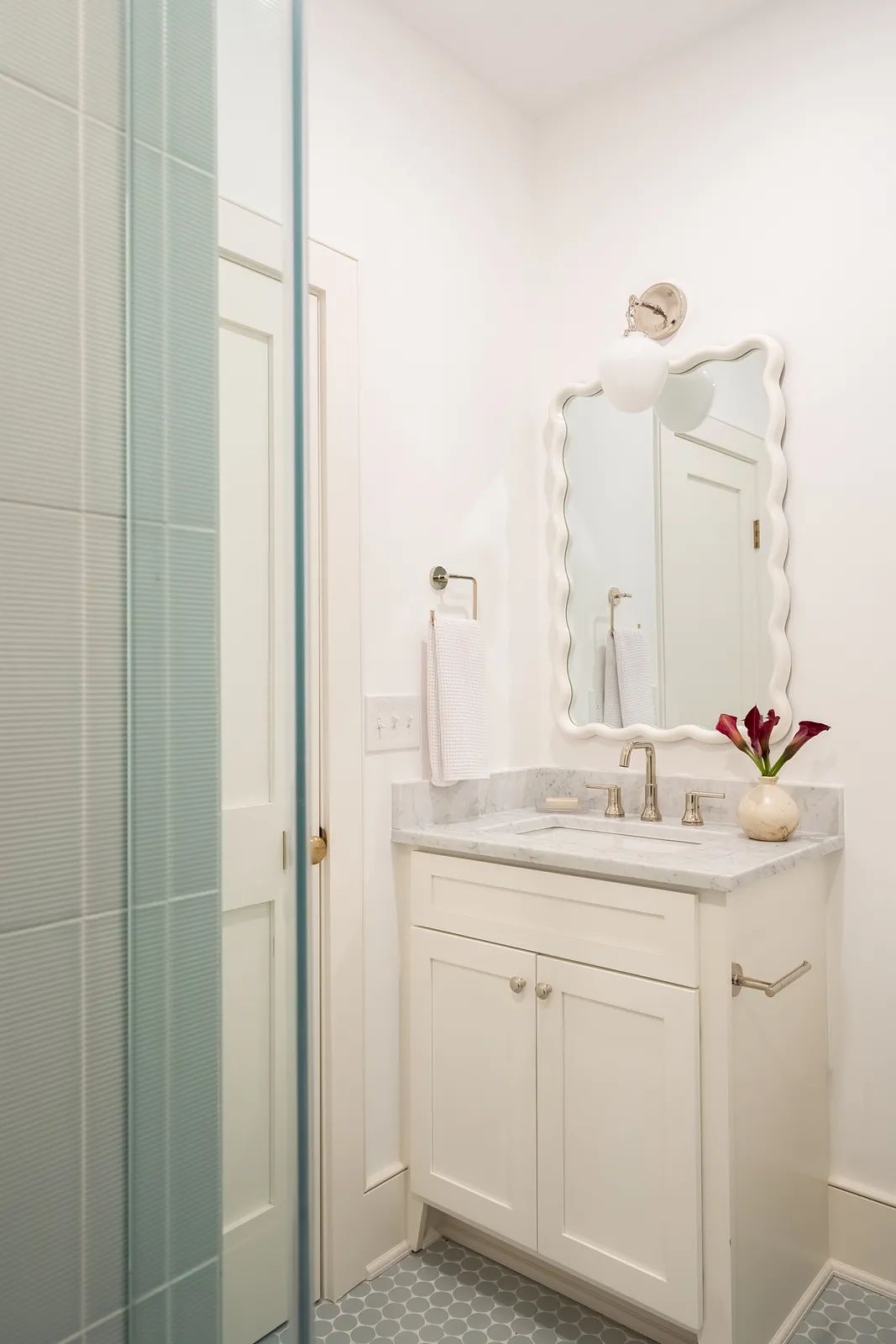 Bathroom with white vanity, marble countertop, round mirror, hexagonal tile floor, and glass shower enclosure