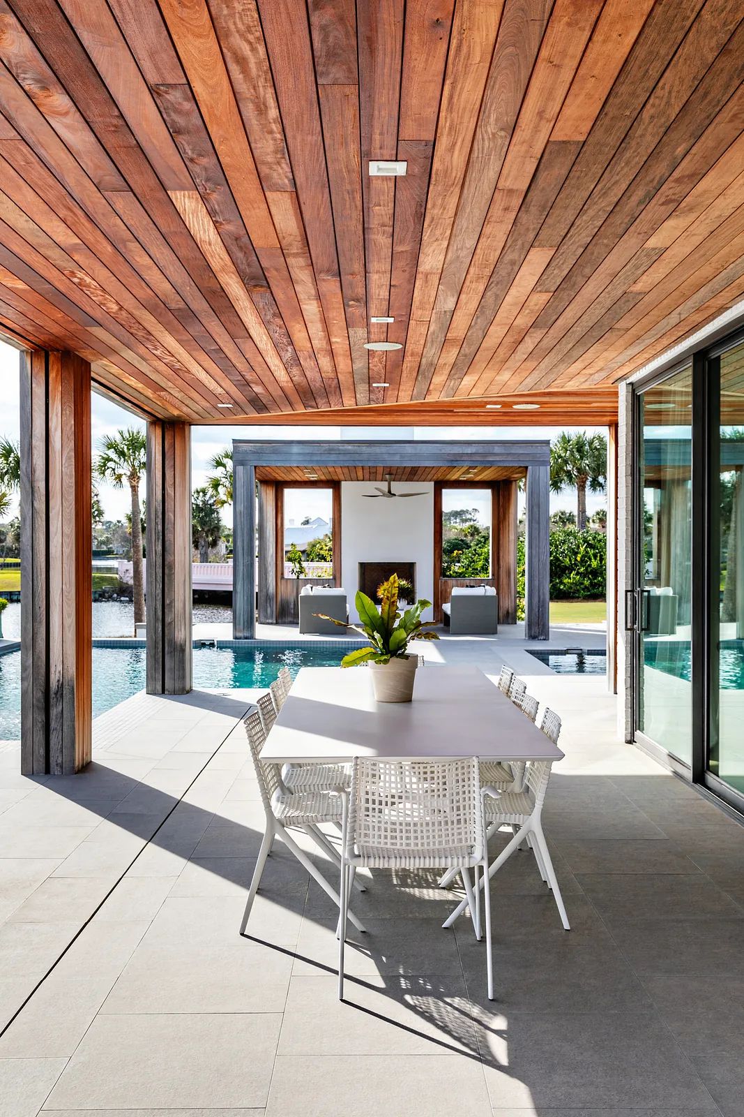 Patio with white dining table, wicker chairs, wooden beams, pool view, and large gray tiled floor.