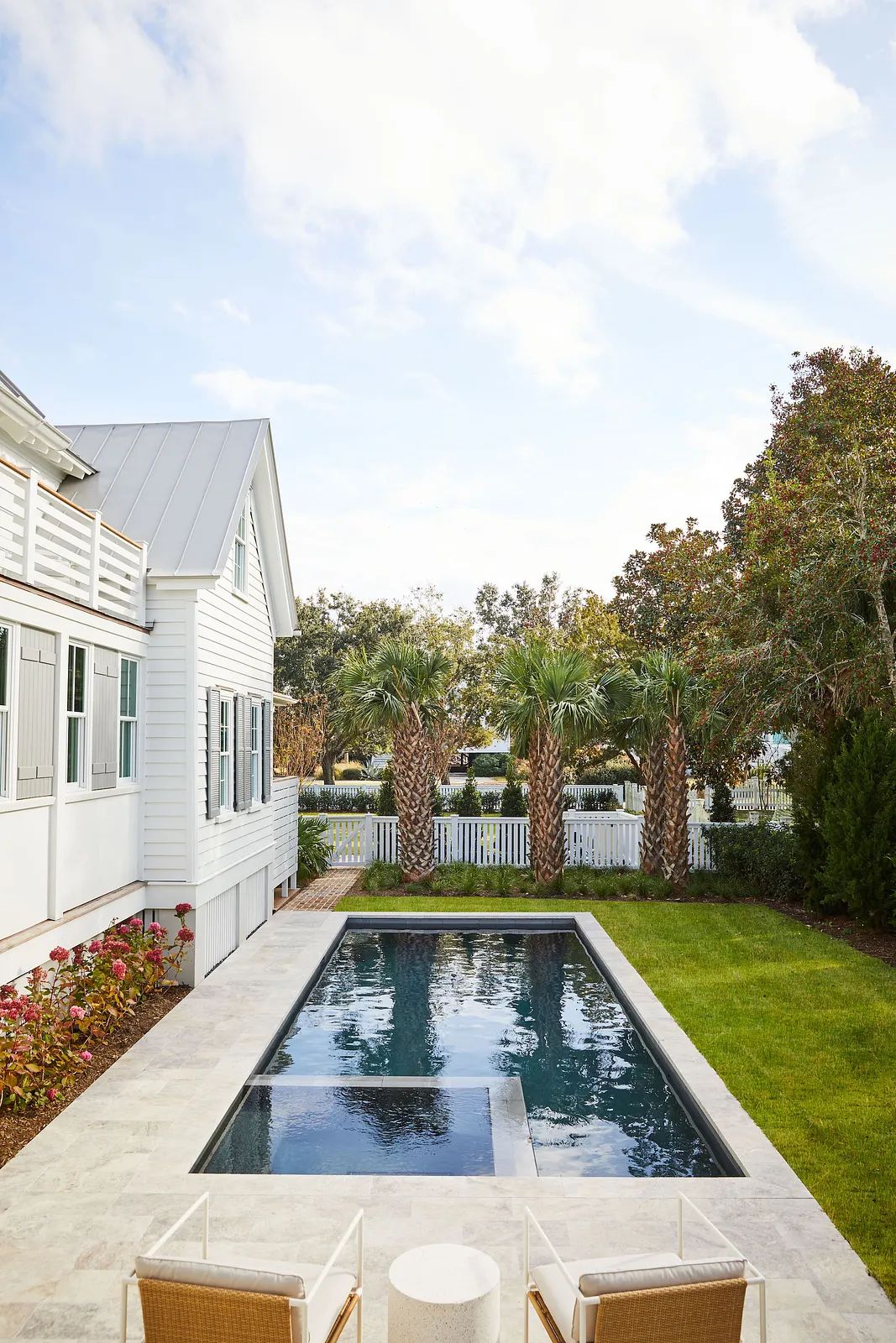 Backyard with rectangular swimming pool, lounge chairs, palm trees, and white fence.