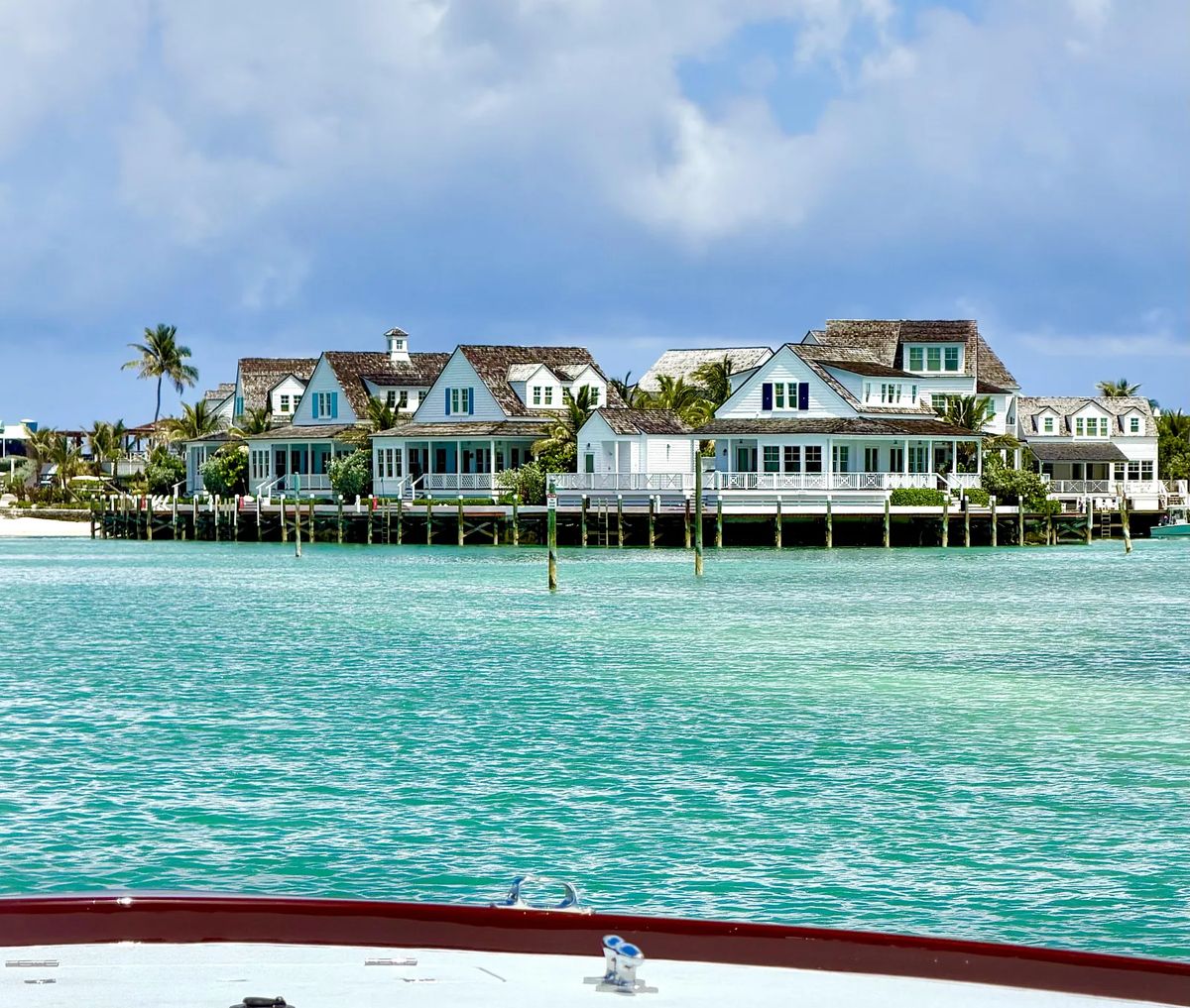 Coastal-style houses along a waterfront with porches, palm trees, and turquoise water.