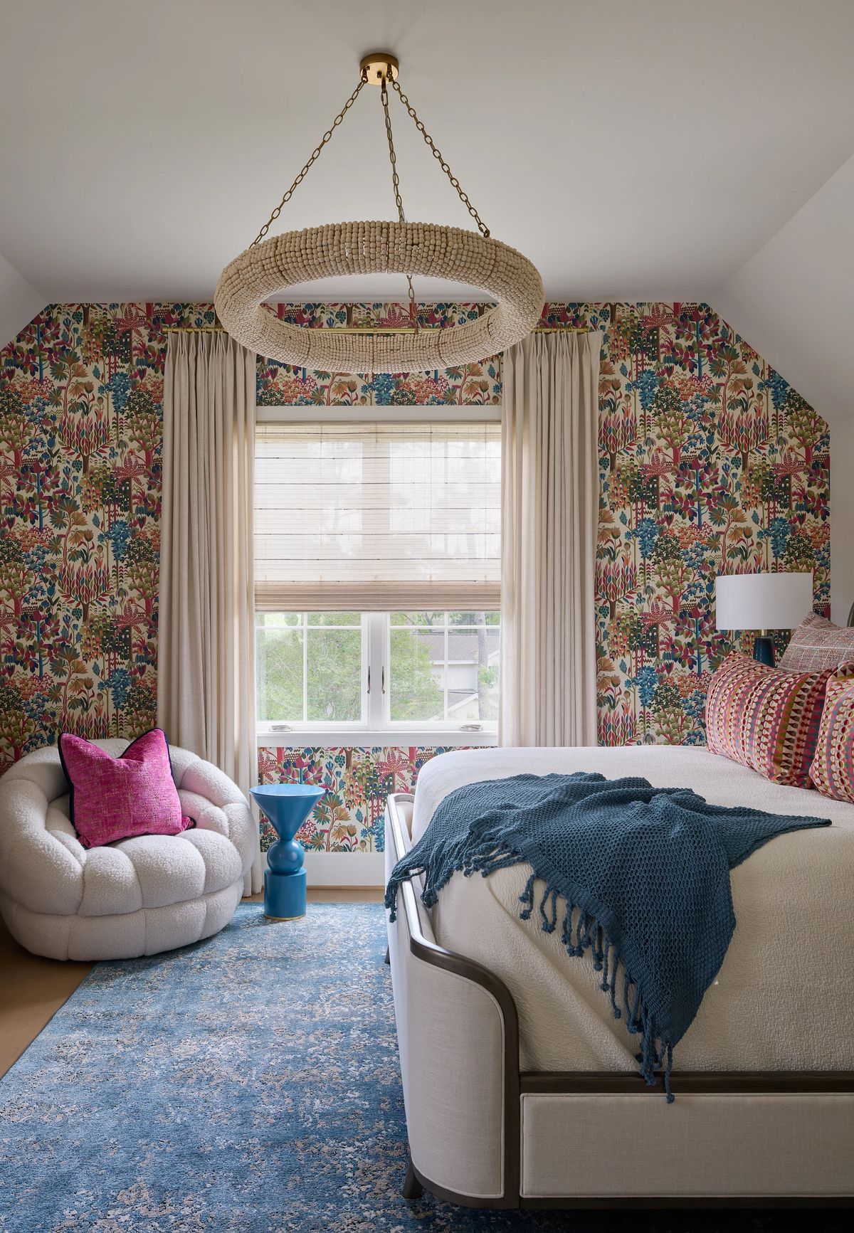 Bedroom with patterned bed, colorful wallpaper, round chandelier, curtains, and plush area rug.