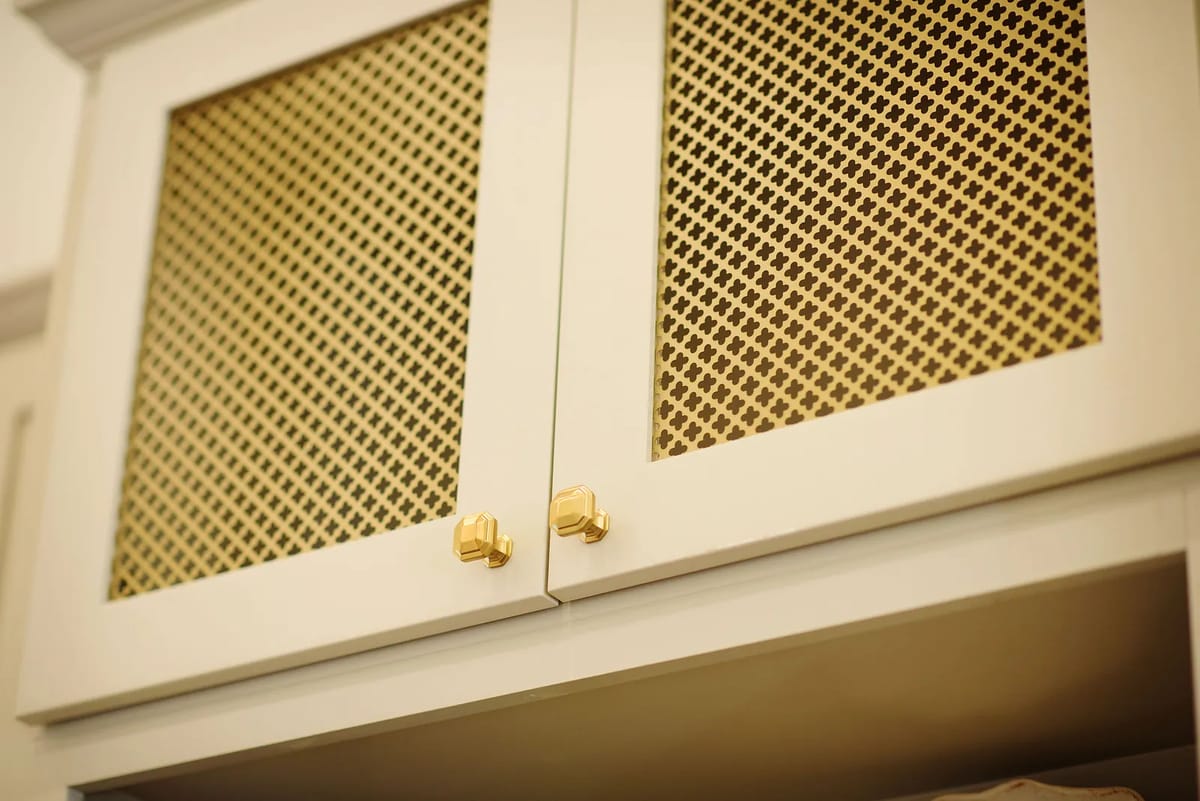 Upper cabinets with light frame and gold mesh doors, part of built-in structure on neutral backdrop.
