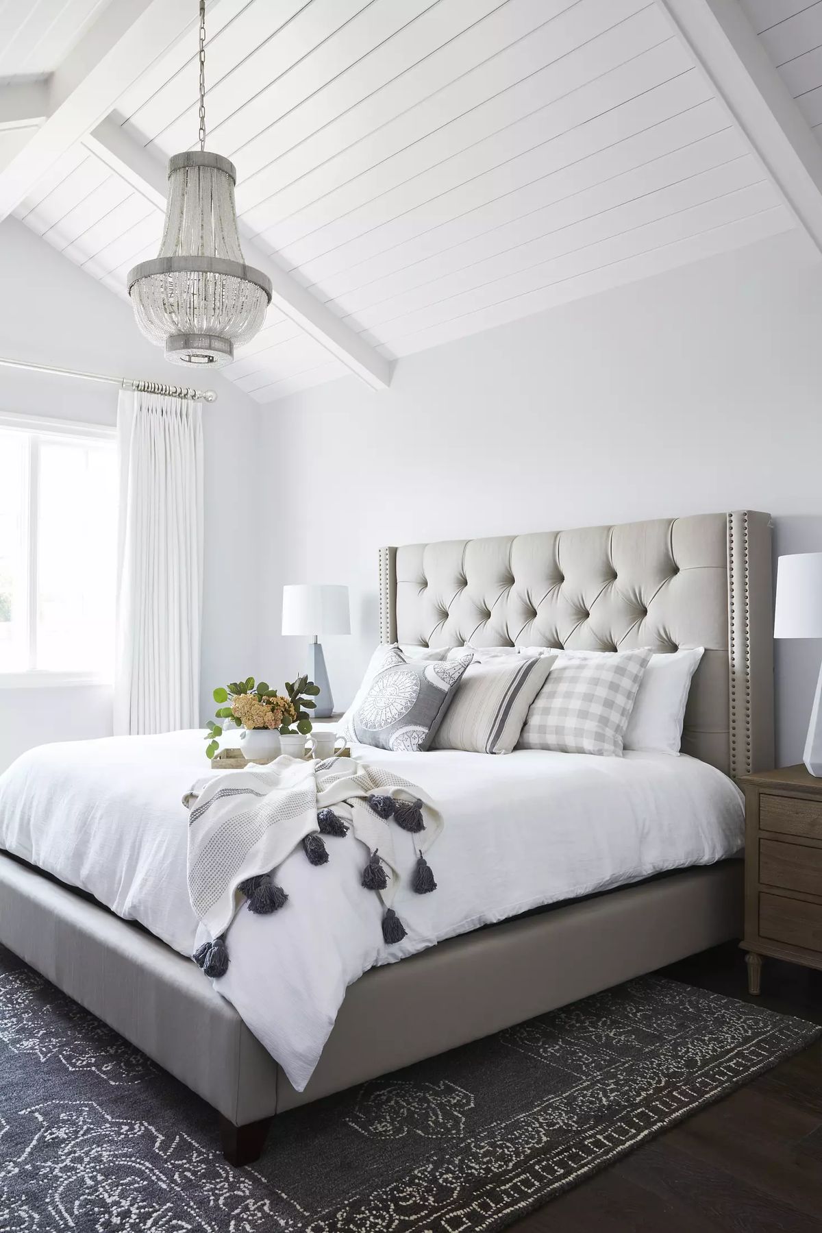 Bedroom with king-sized tufted bed, bedside tables, lamps, decorative throw, and vaulted ceiling with beams.