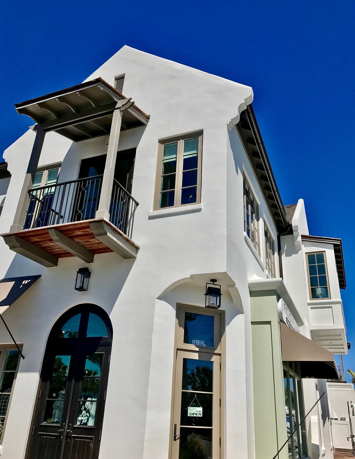 Exterior view of a two-story building with white stucco, balcony, large windows, and decorative lamp.