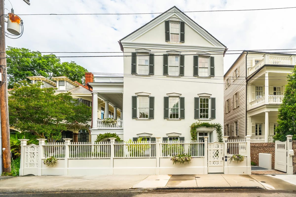 Front exterior of a two-story house with white facade, black shutters, and decorative fence.