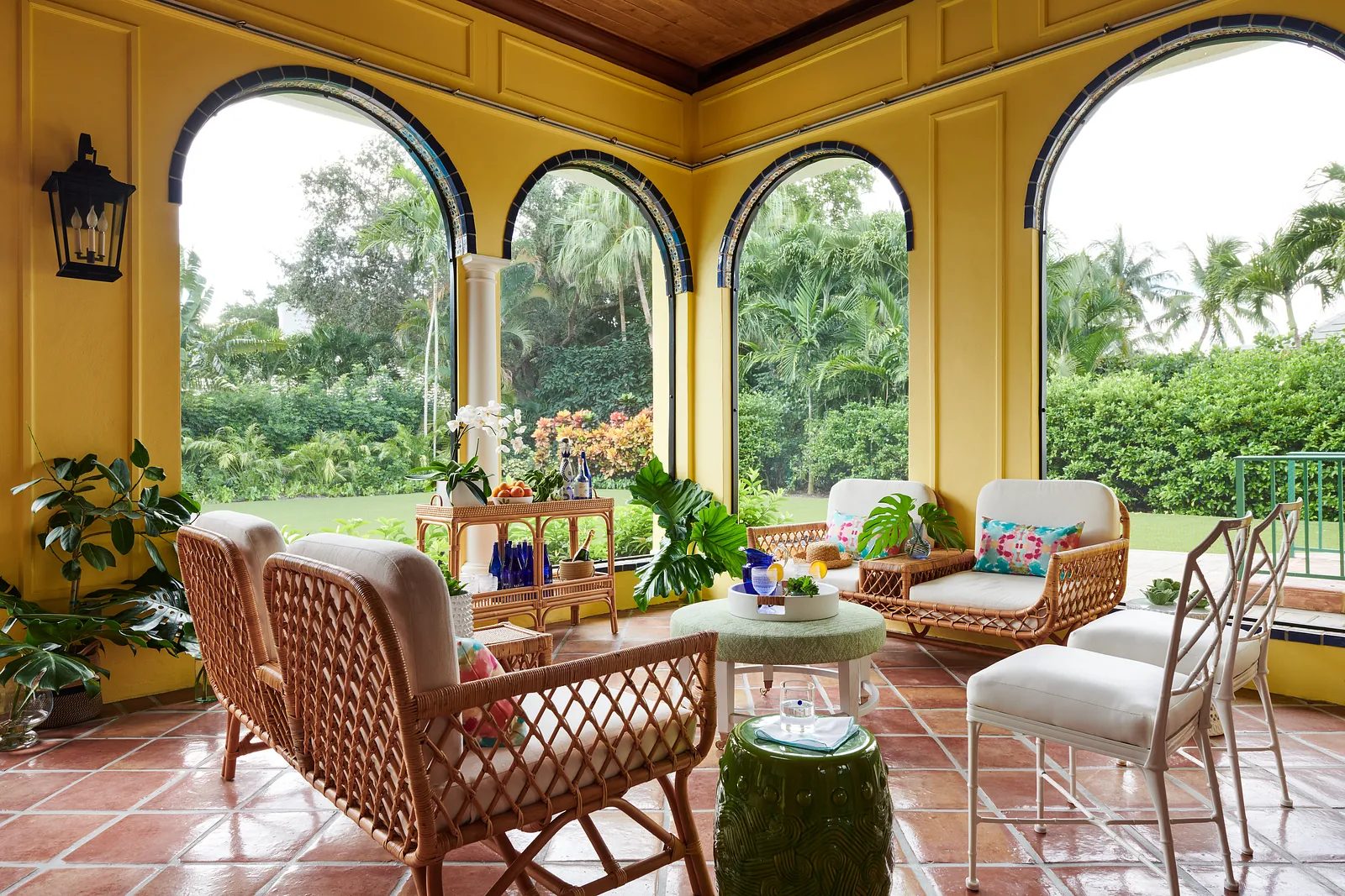 Patio with wicker chairs, glass table, wheeled tray, potted plants, and large arched windows.
