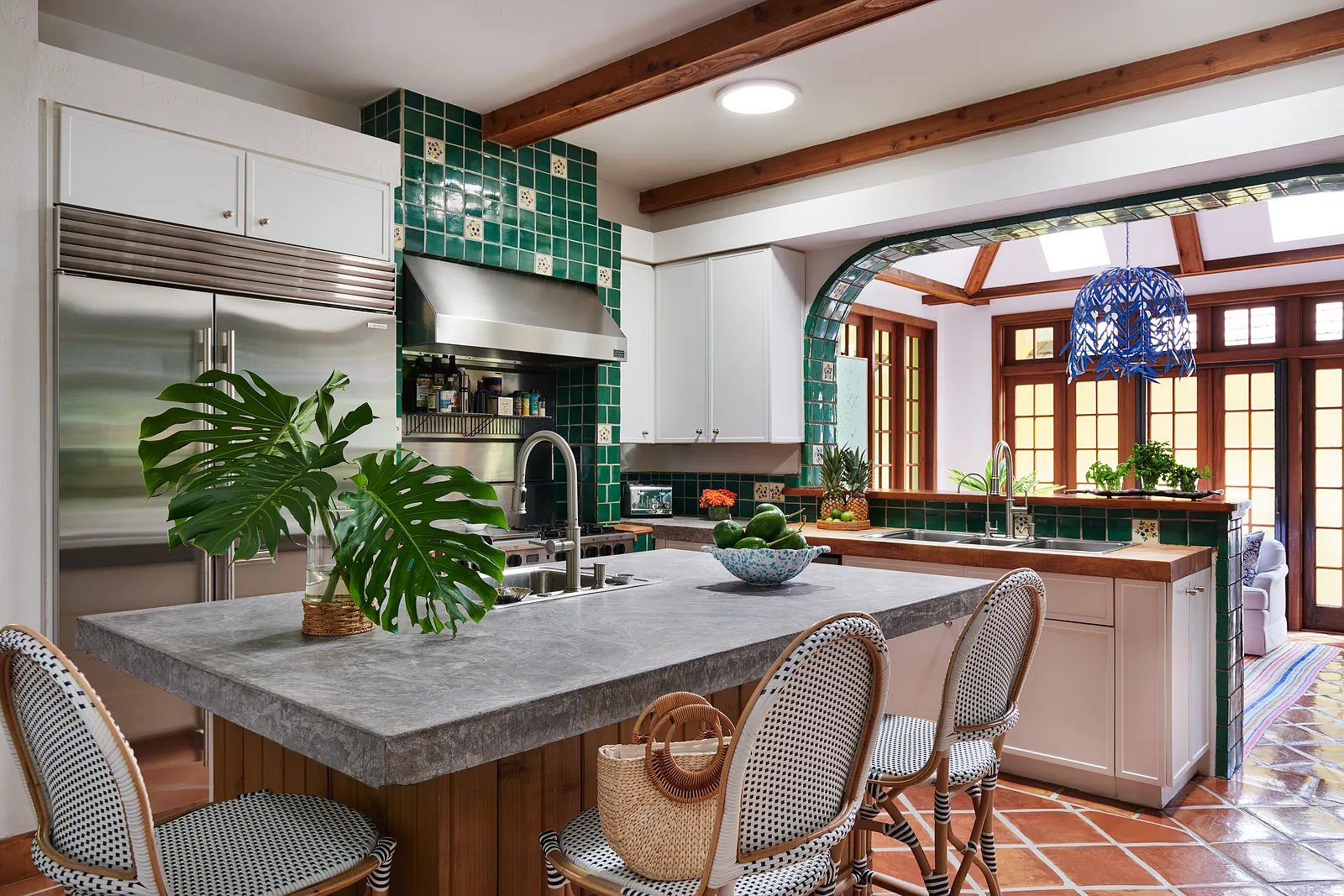 Kitchen with gray stone island, green tiled backsplash, stainless steel appliances, and wooden beams.