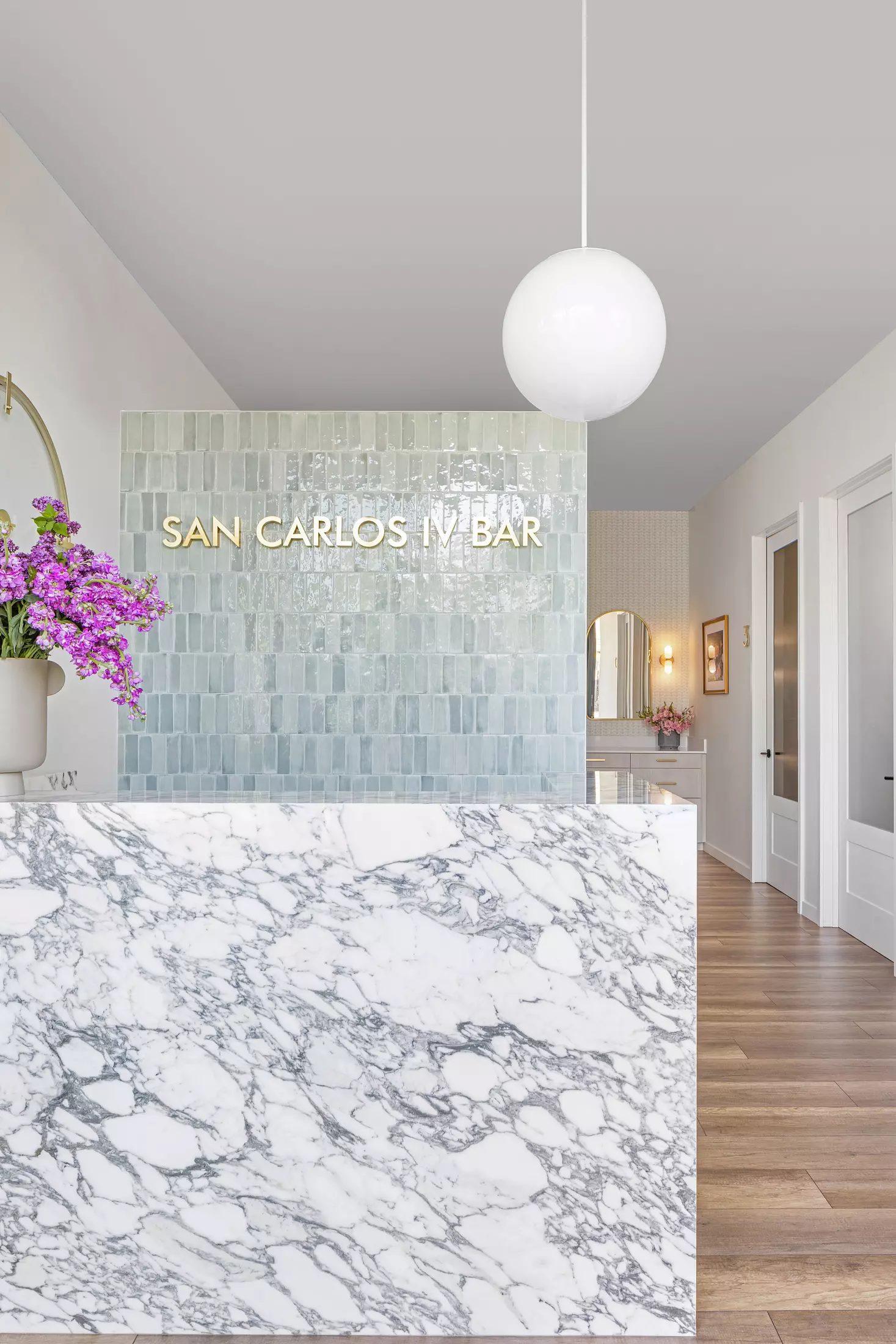 Bar area with marble countertop, pastel tiles, purple flowers, and signage.