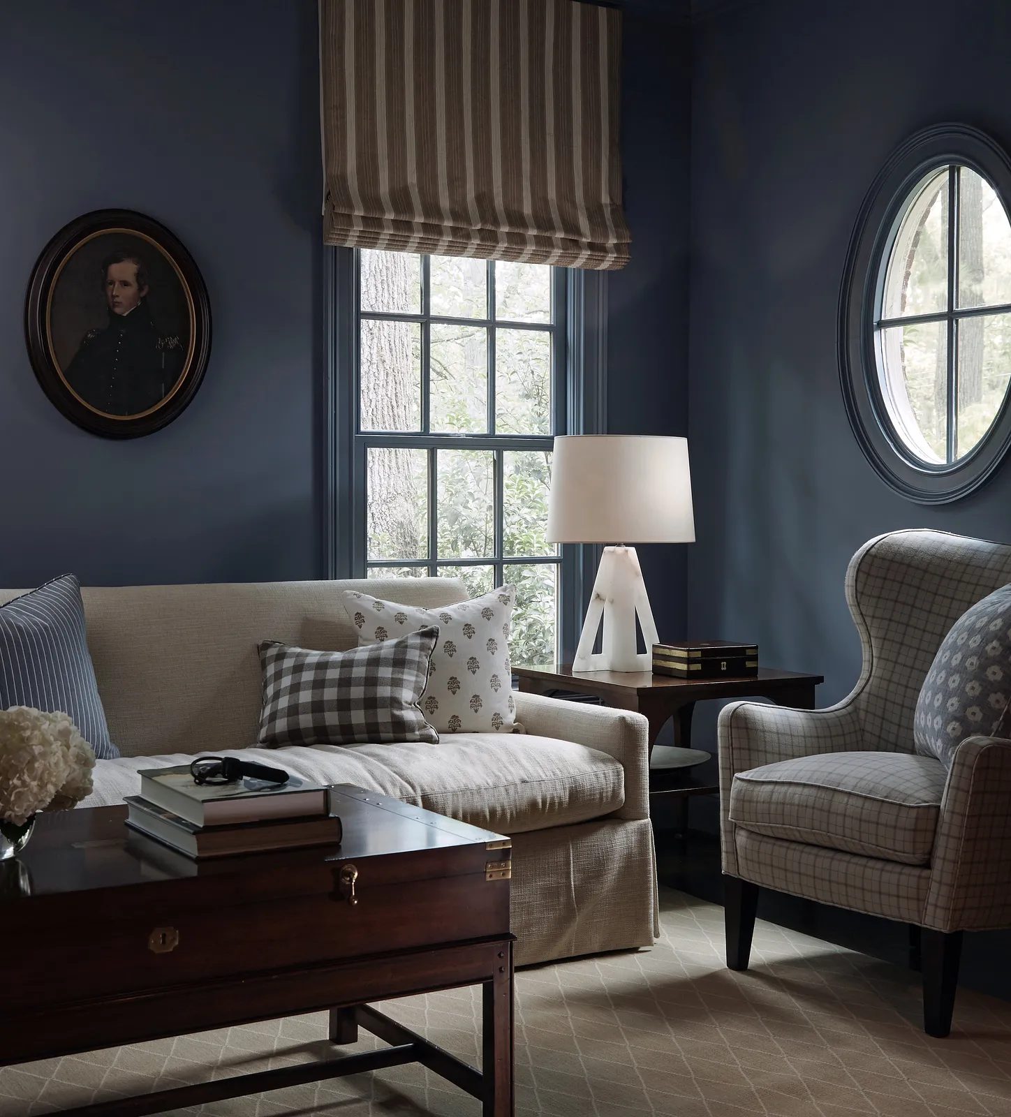 Living room with beige sofa, coffee table, checkered pillow, upholstered armchair, and blue walls with windows