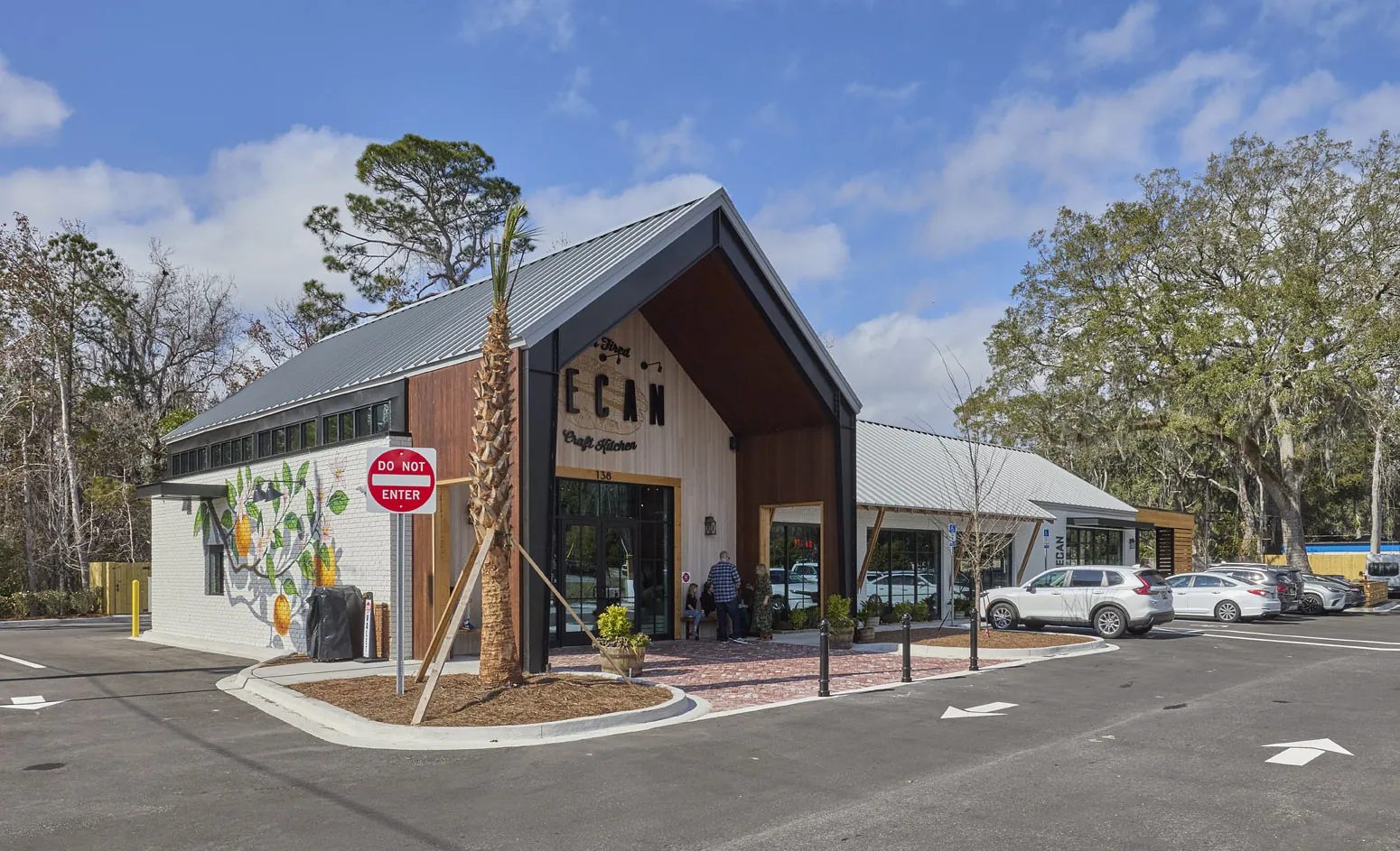 Exterior view of a modern building with sloped roof, large windows, palm trees, and paved parking.