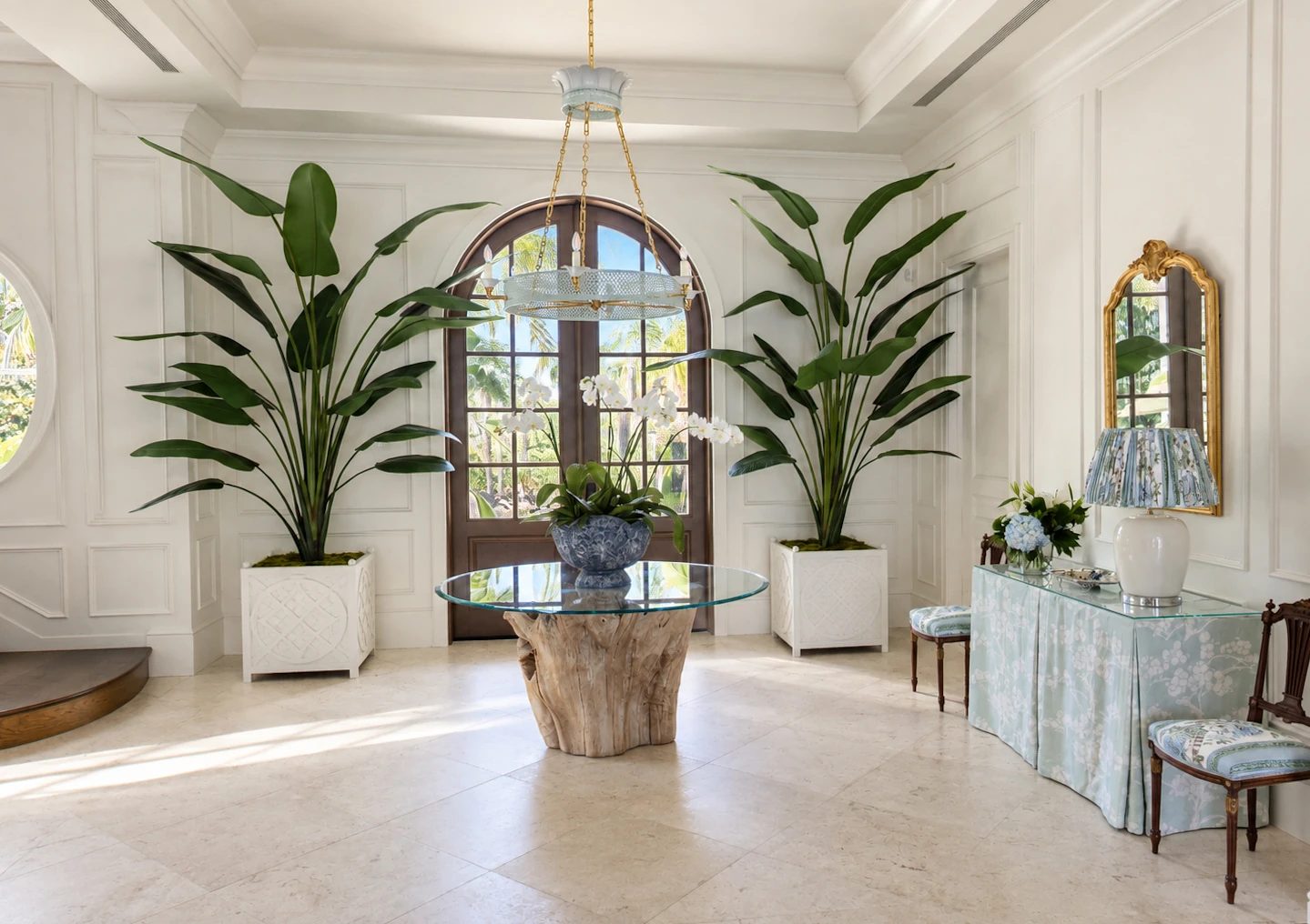 Foyer featuring a round glass table, large windows, potted plants, console table, and decorative mirror.