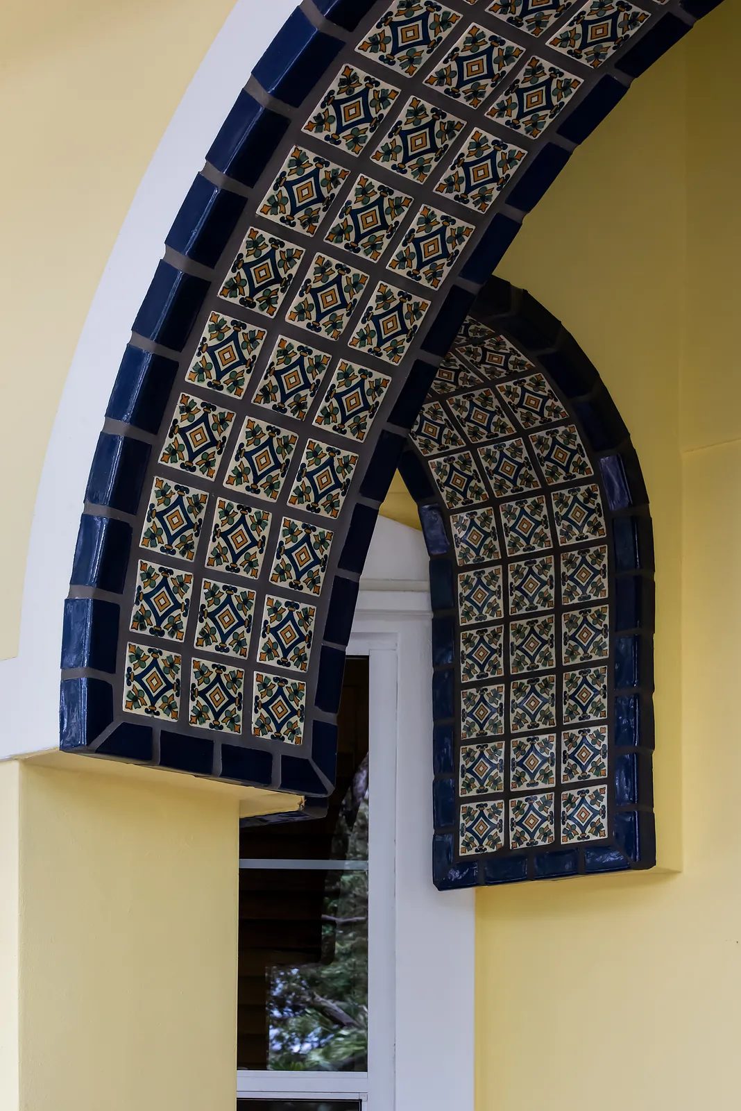 Exterior view with arched openings, blue and yellow tile work, and white framed windows.