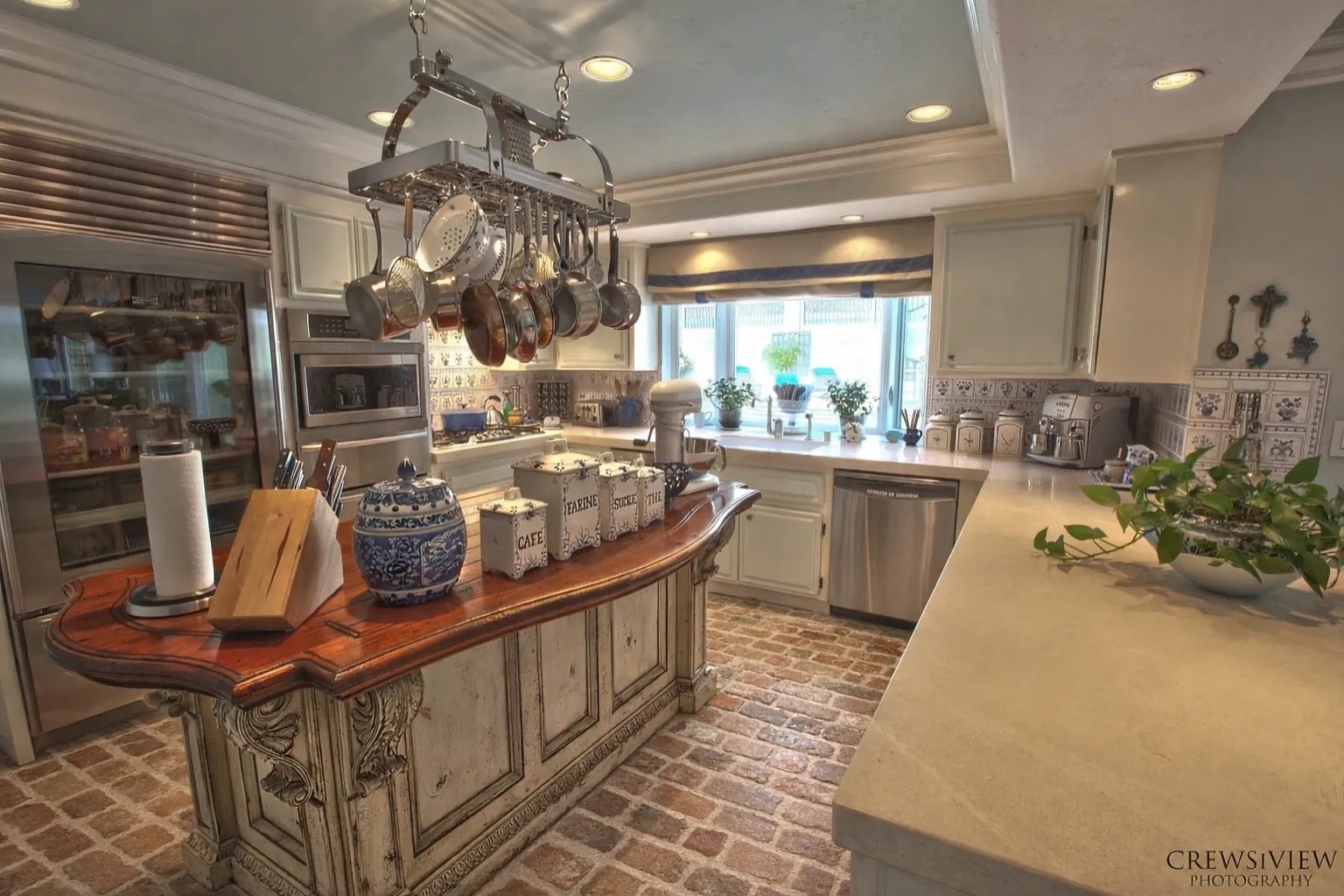 Kitchen with island, stainless steel appliances, pot rack, white cabinets, and decorative tiles.