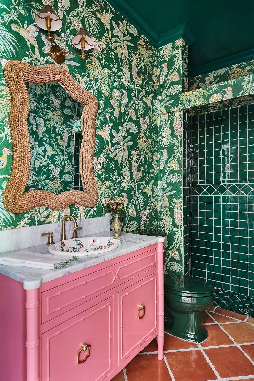 Bathroom with pink vanity, marble countertop, green toilet, tropical wallpaper, and terracotta tile floor