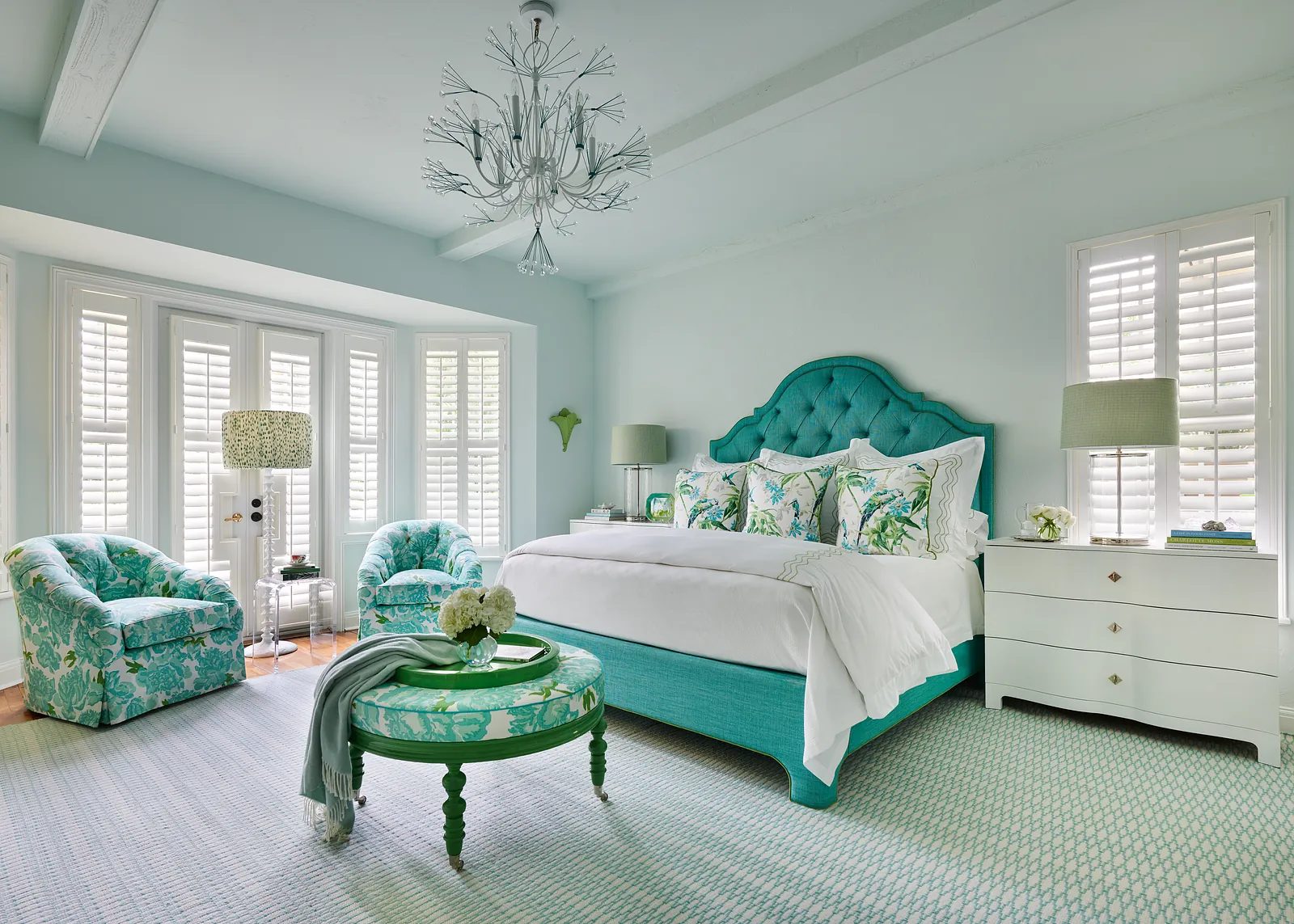 Bedroom with turquoise bed, patterned armchairs, green coffee table, white dresser, and light blue walls