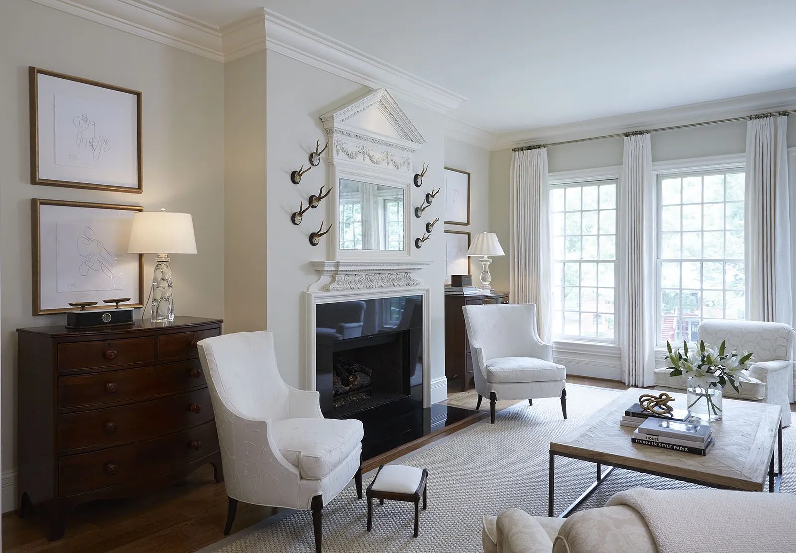 Living room with armchairs, coffee table, dresser, fireplace, mirror, artwork, and large windows with curtains