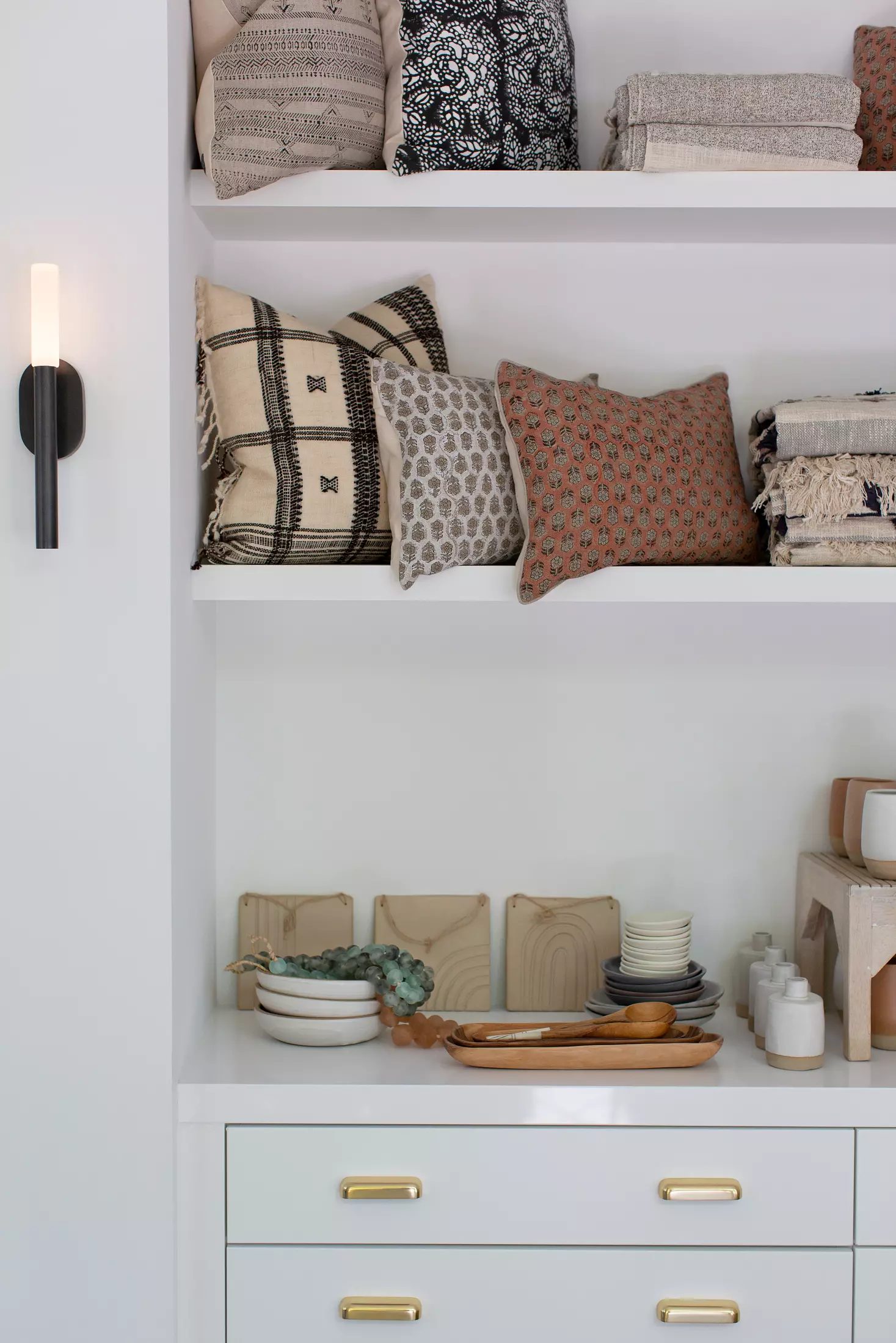 Butler's pantry with open shelving, textiles, ceramics, wooden trays, and brass-handled cabinetry.