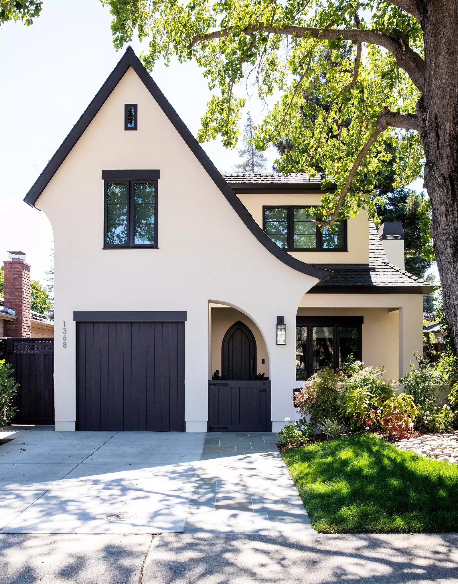 Exterior front of a house with white stucco, dark trim, arched entryway, and landscaped garden.