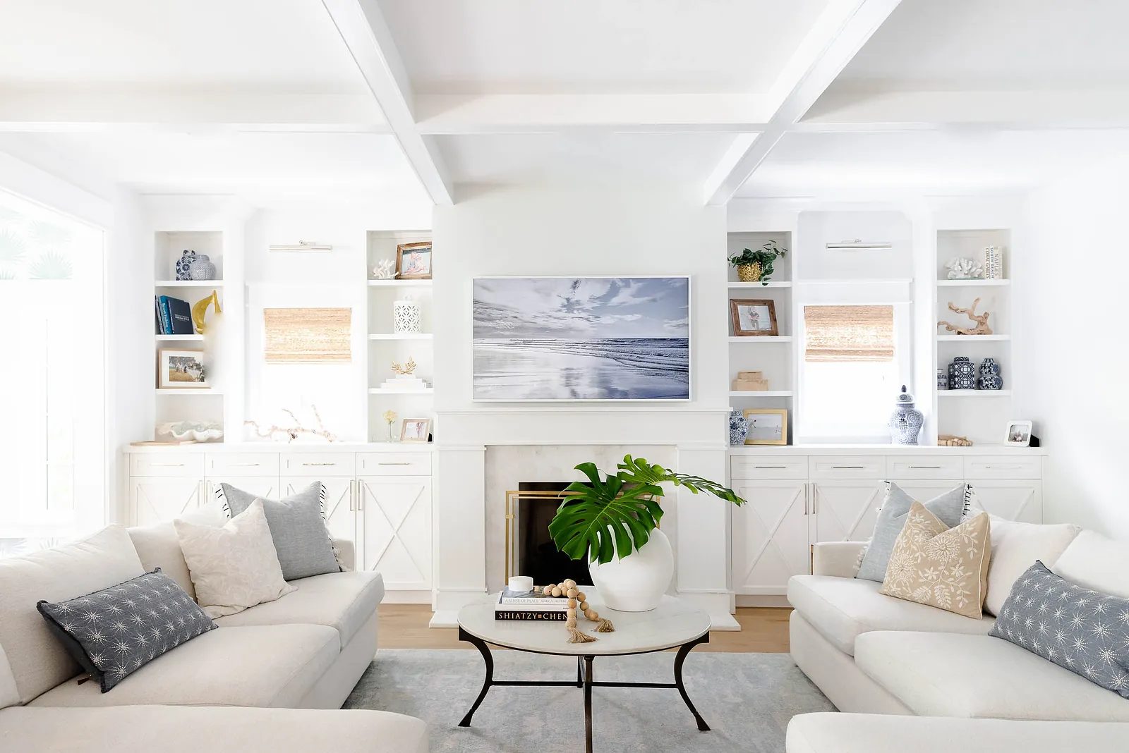 Living room with white sofas, round coffee table, built-in shelves, television, and green plant.