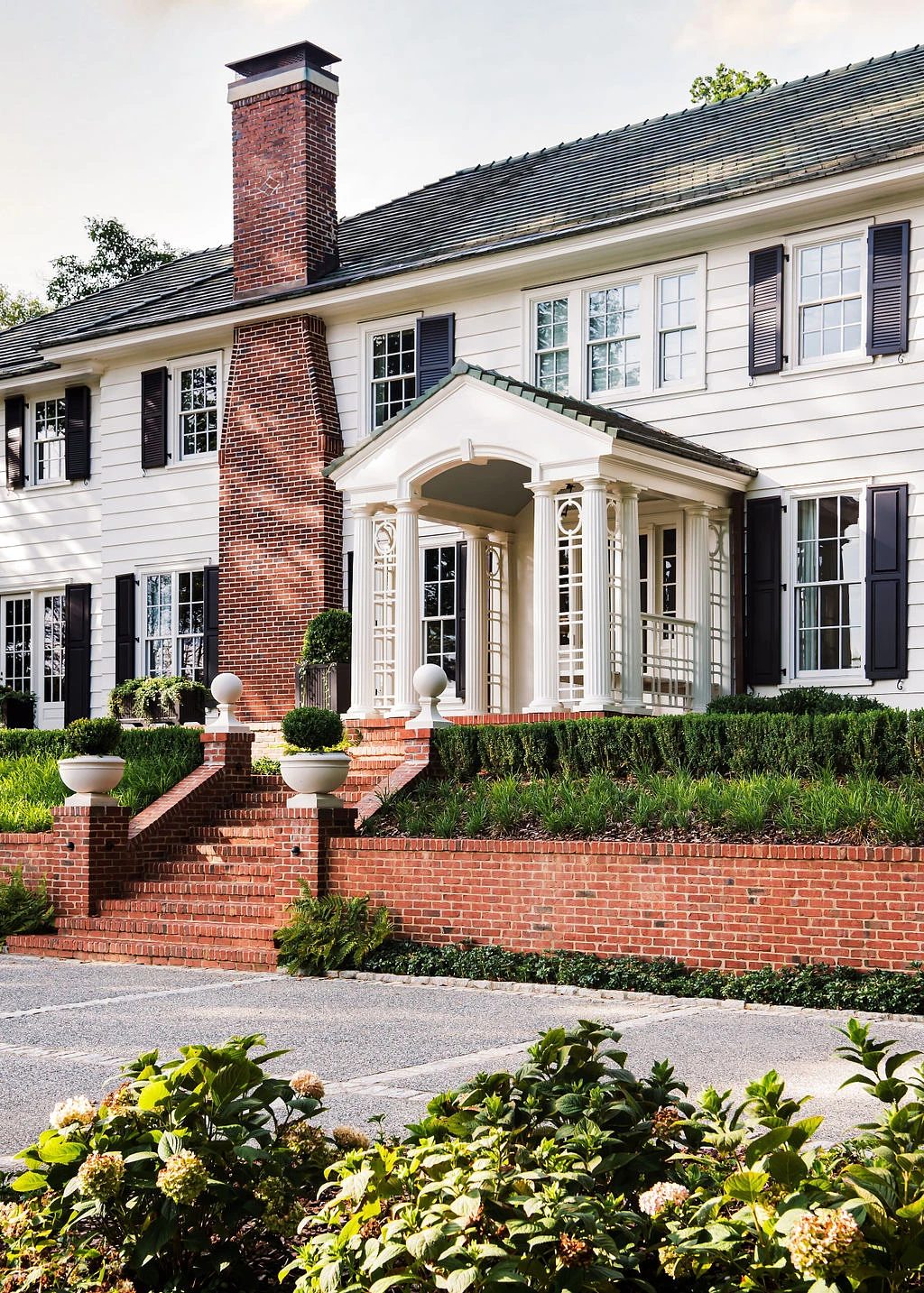 Exterior front view of a two-story house with portico, brick steps, and landscaped garden.