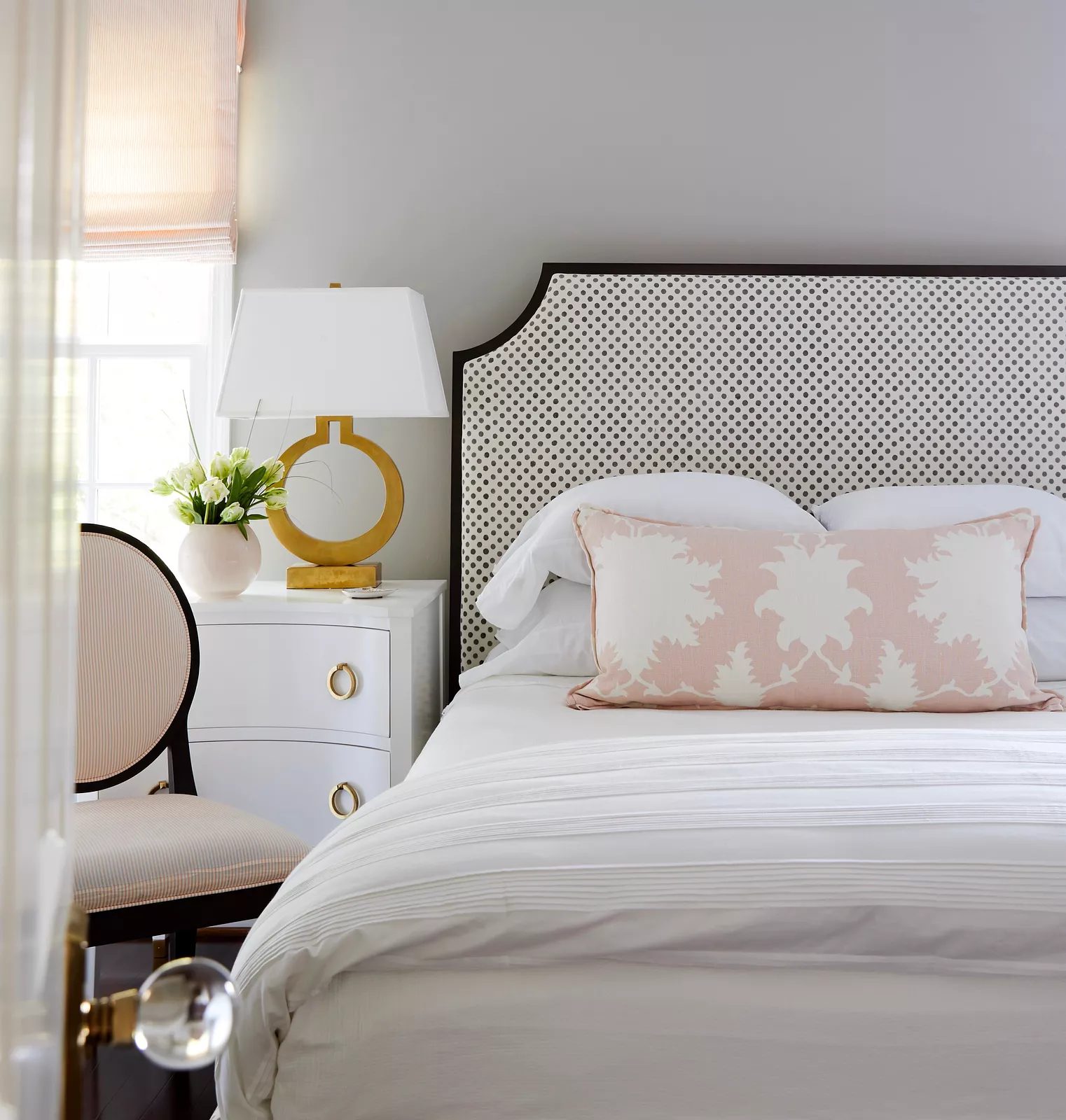 Bedroom with patterned headboard, white bedding, nightstand, table lamp, and chair in the corner.