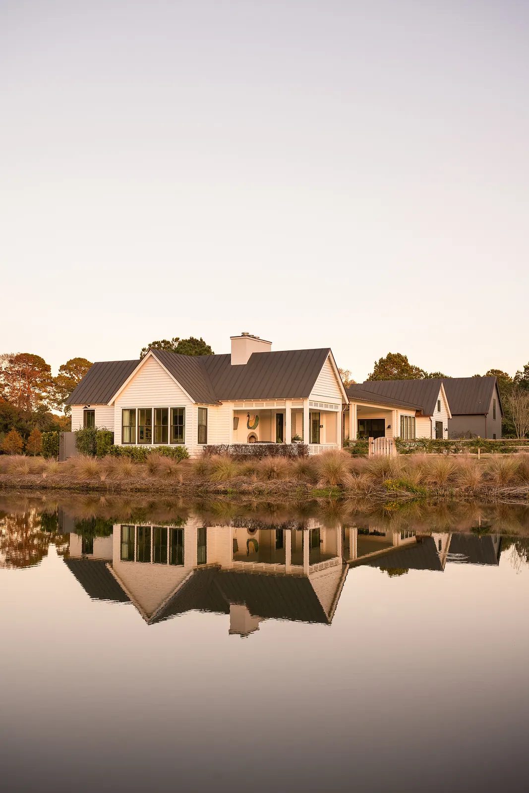 Front exterior view of a house with metal roof, wooden siding, large windows, and a reflecting pond.