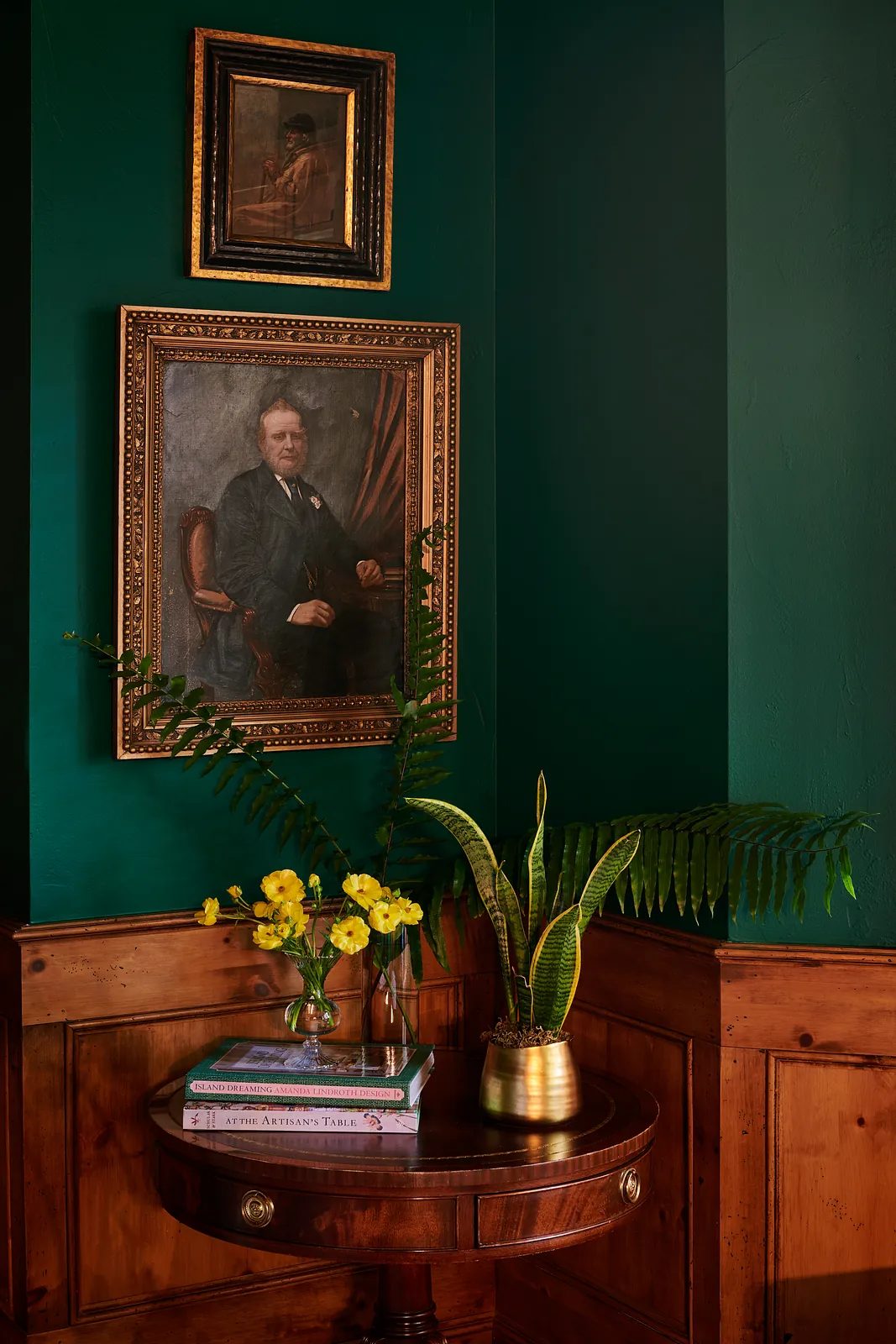 Corner area with dark green wall, round table, portrait, flowers, and decorative plant.