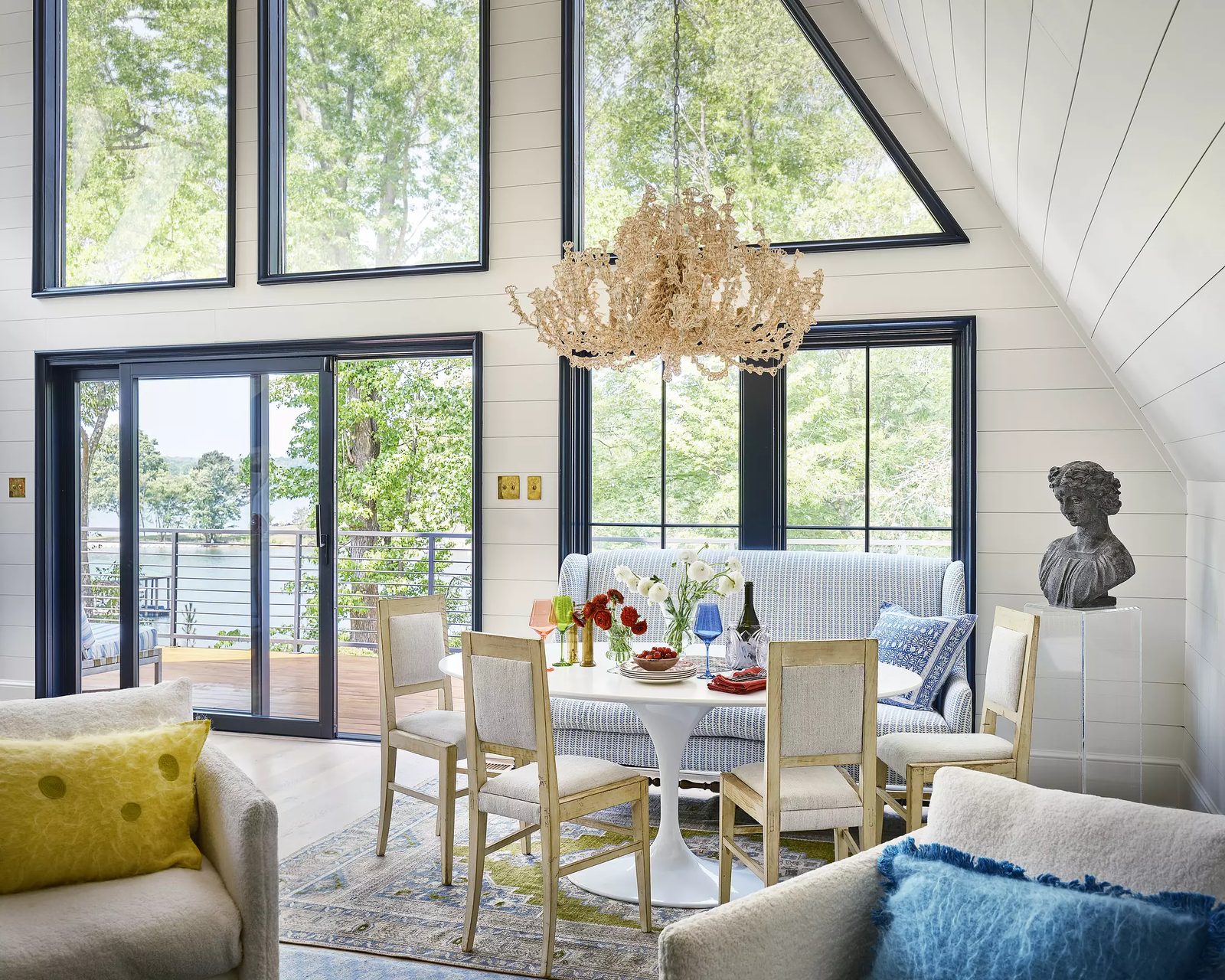 Dining room with round table, wooden chairs, blue sofa, large chandelier, and shiplap walls.