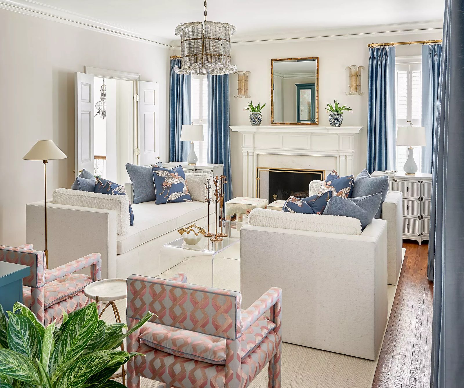 Living room with white sectional sofas, patterned armchairs, glass coffee table, and a fireplace.