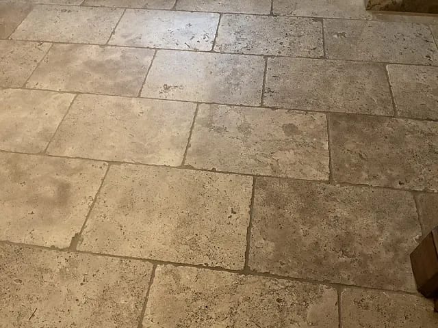 Close-up of a textured stone floor with large rectangular tiles and faint grout lines.