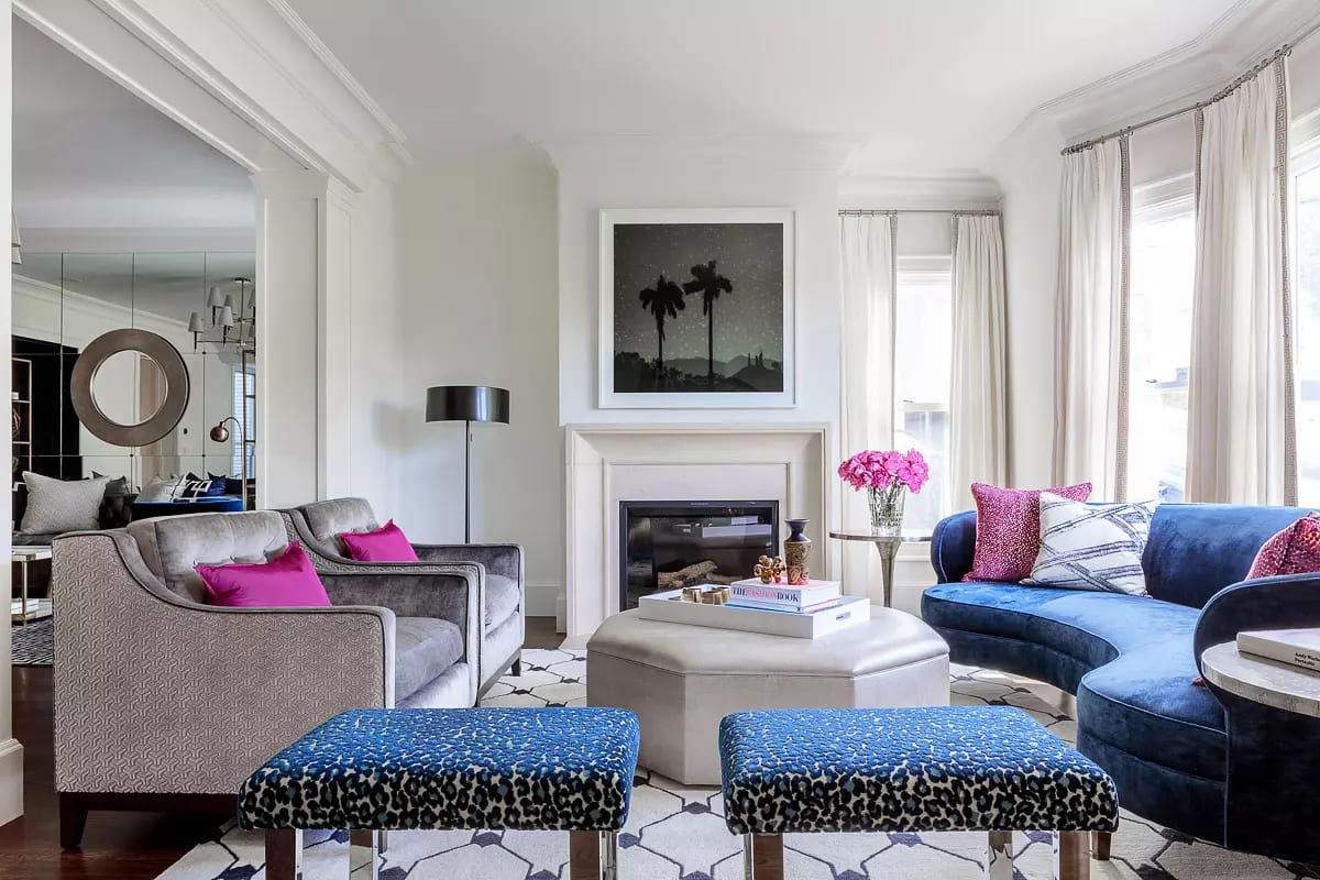 Living room with gray sofa, blue curved couch, ottoman, coffee table, fireplace, and large windows.