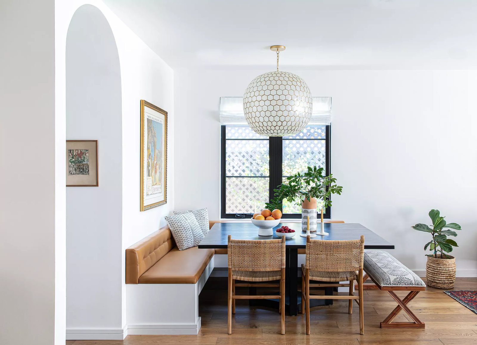 Dining room with dark wood table, leather bench, wicker chairs, pendant light, and framed artwork.