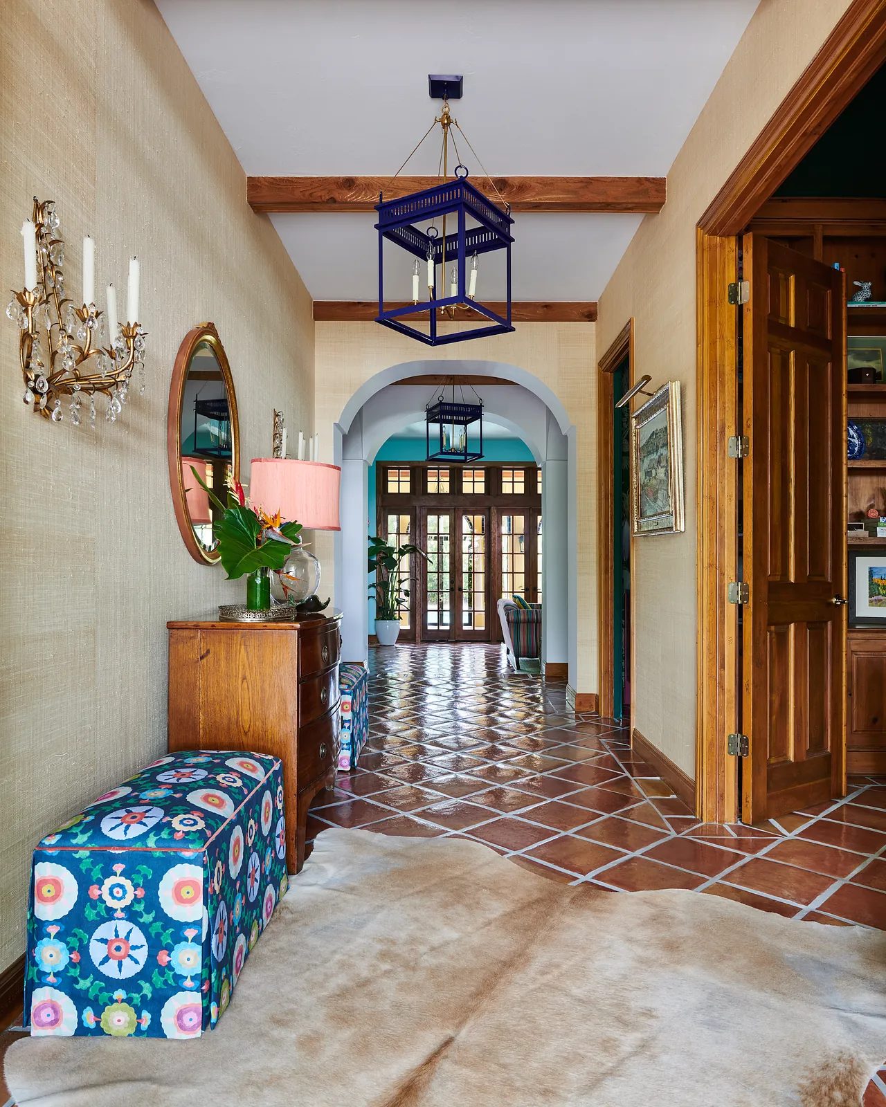 Hallway with console table, colorful ottoman, mirror, and beige area rug with tiled floor.
