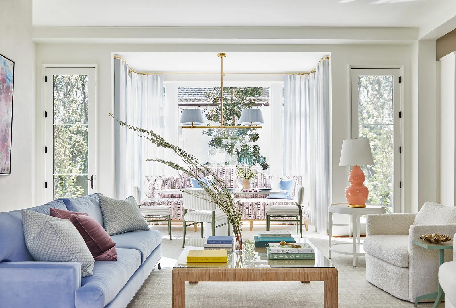 Living room with light blue sofa, white armchair, glass coffee table, large windows, and patterned chairs.