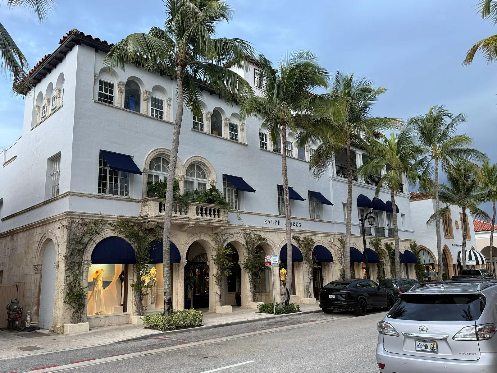 Building exterior with arches, blue awnings, white walls, and palm trees.
