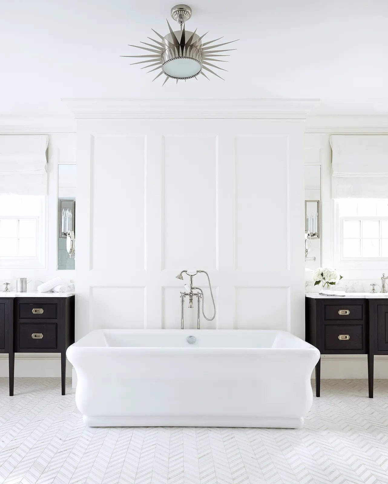 Bathroom with freestanding bathtub, dark wood vanities, herringbone floor, and white paneling.