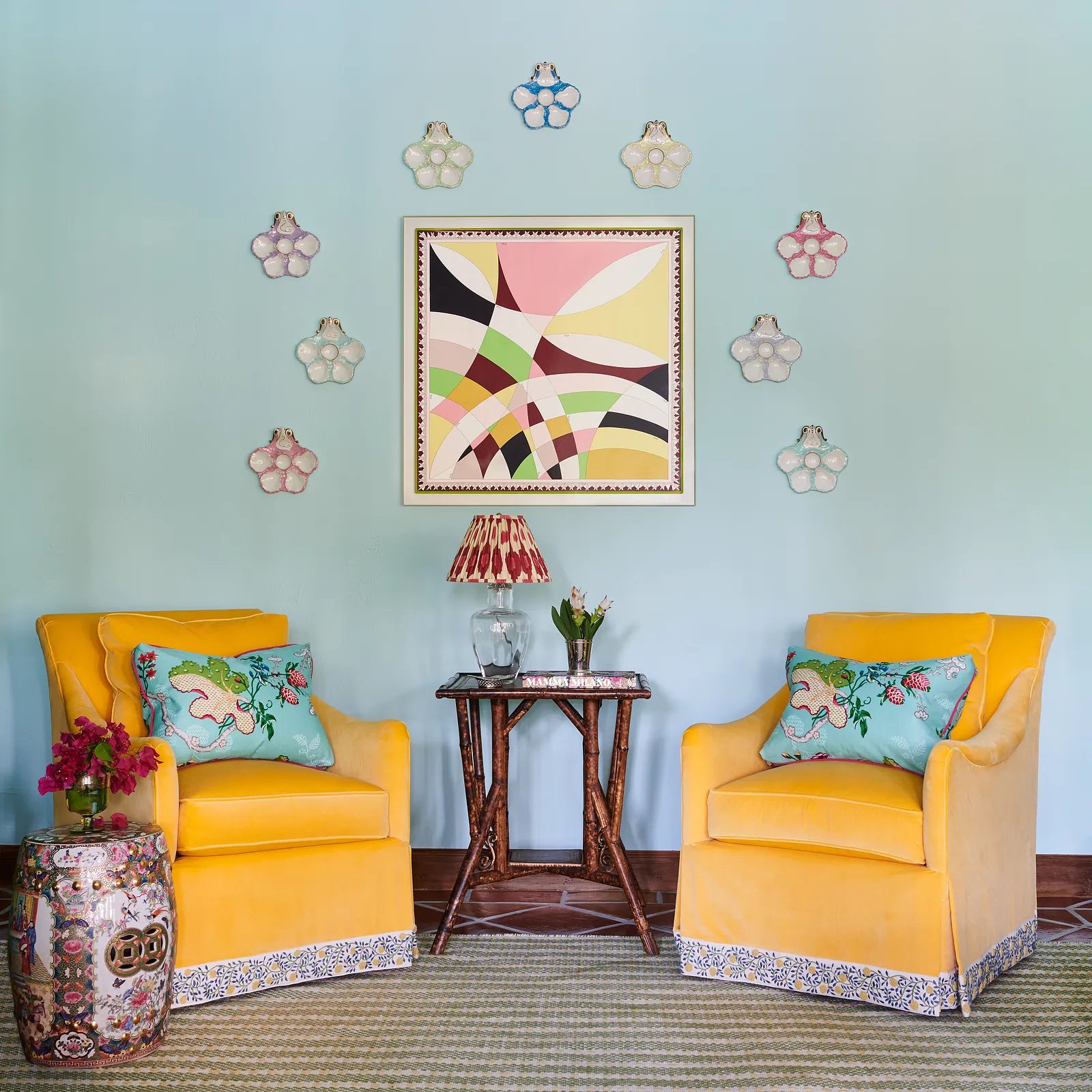 Seating area with yellow armchairs, a small table, a painting, and decorative light fixtures on a blue wall.