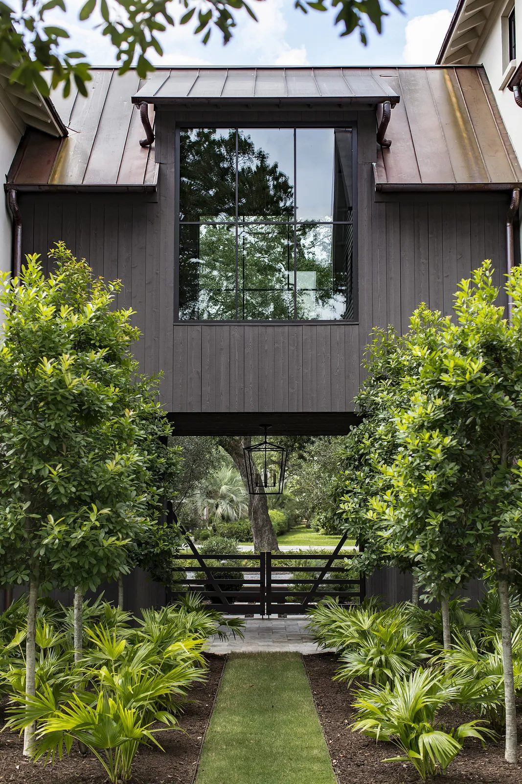 Exterior front view of a structure with dark wood siding, large window, and landscaped pathway.
